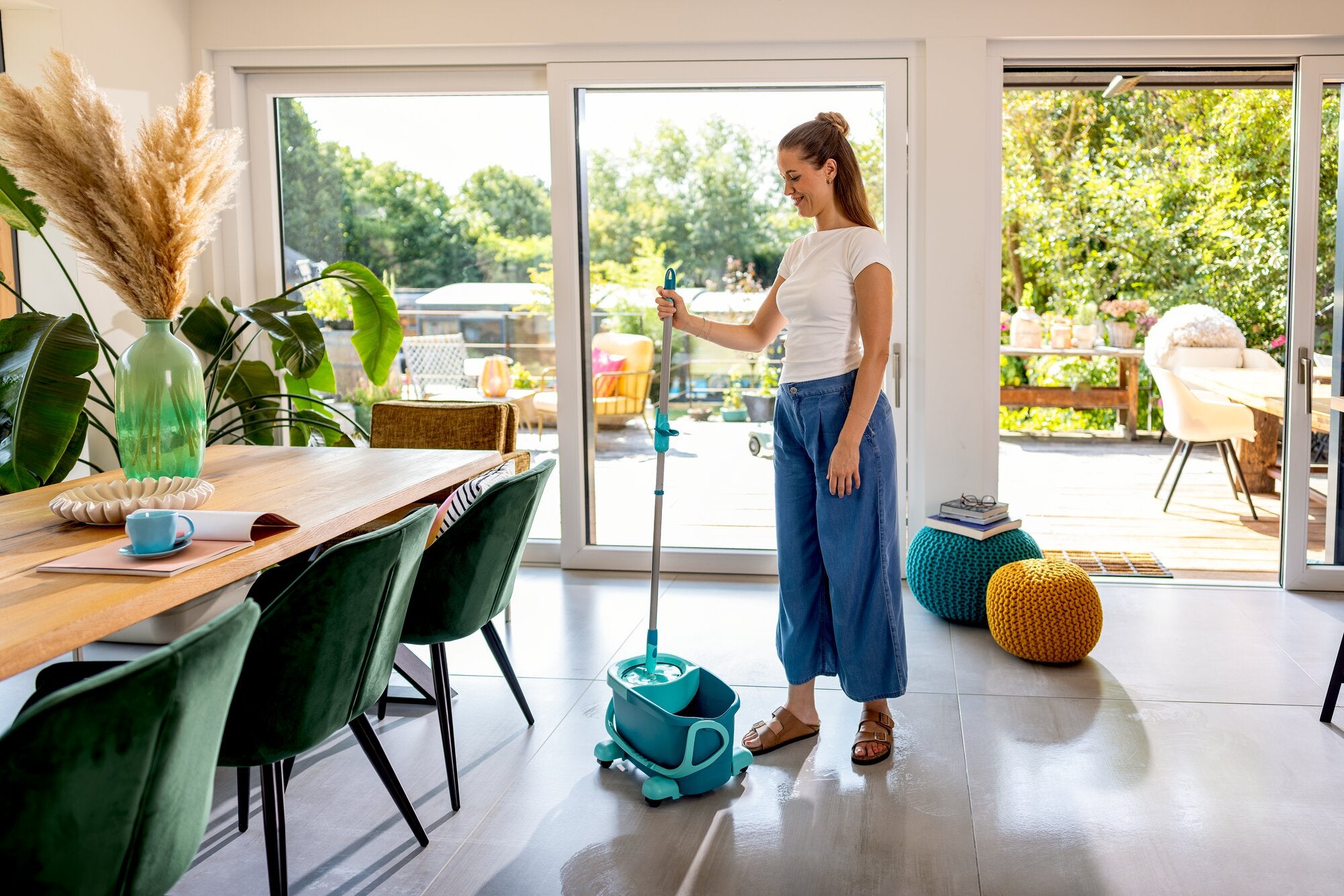 Leifheit CLEAN TWIST Disc Mop Mobile Lavapavimenti-Set in Türkis, im hellen Wohnraum von einer Frau genutzt; Eimer mit Schleudersystem und Stiel sorgen für komfortables Wischen auf glatten Böden.