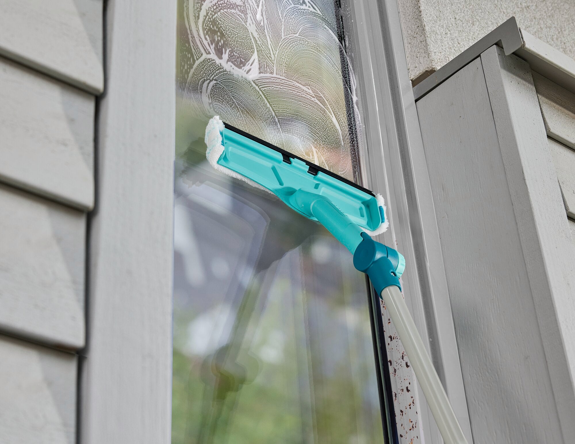 Ein Fensterreiniger mit Teleskopstange wird verwendet, um ein Fenster zu säubern. Der Reiniger hat eine türkisfarbene Halterung und entfernt effektiv Schmutz.