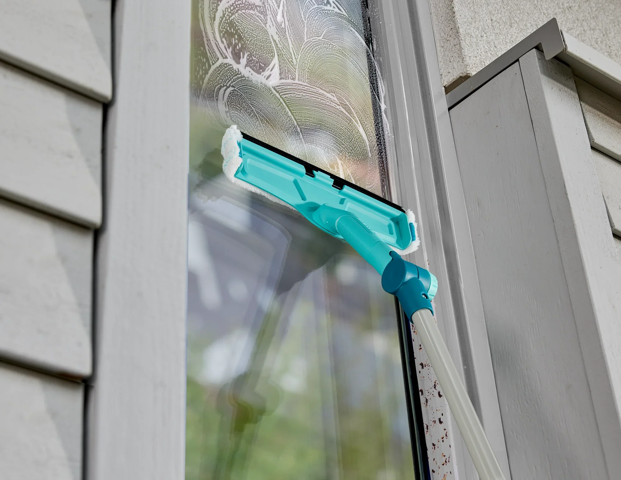Een raamreiniger met telescoopstang wordt gebruikt om een raam schoon te maken. De reiniger heeft een turquoise gekleurde houder en verwijdert vuil effectief.