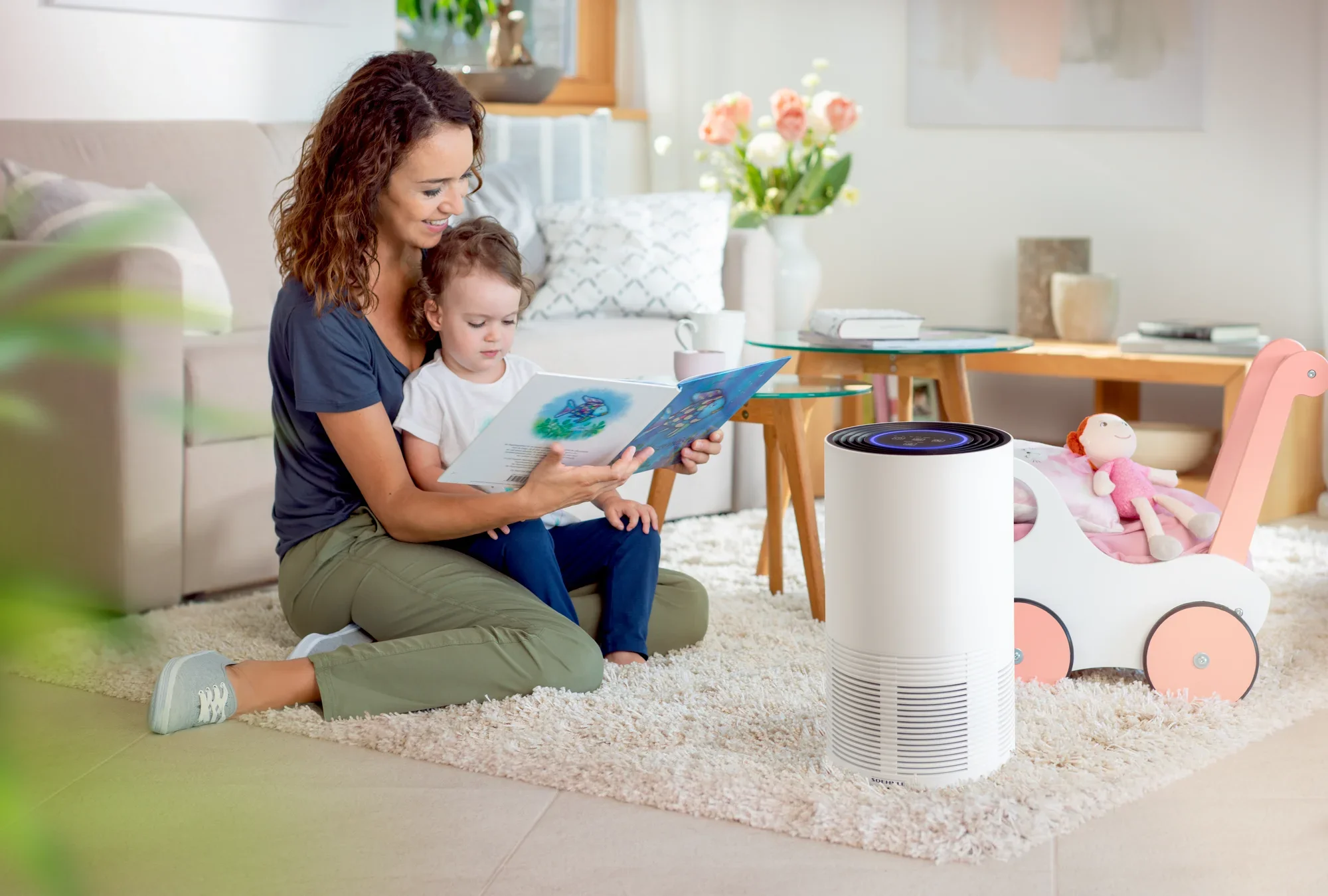 Matka czyta dziecku książkę w salonie. Na pierwszym planie znajduje się oczyszczacz powietrza Airfresh Clean 400, który zapewnia czyste i świeże powietrze.