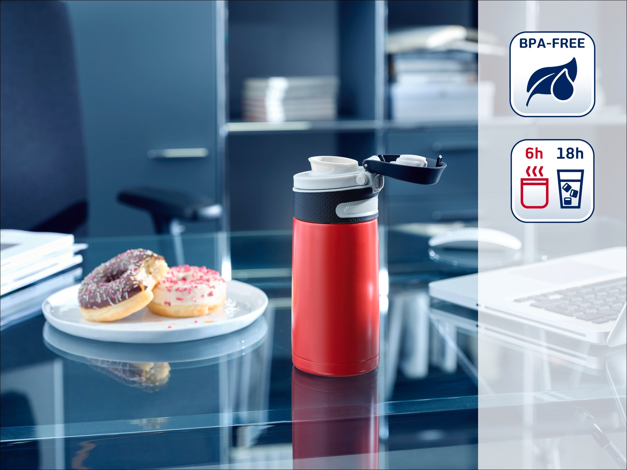 Thermos rouge sur un bureau, couvercle ouvert, à côté une assiette avec des beignets. À l'arrière-plan, une étagère de bureau. Sans BPA, garde les boissons chaudes pendant 6 heures et froides pendant 18 heures.