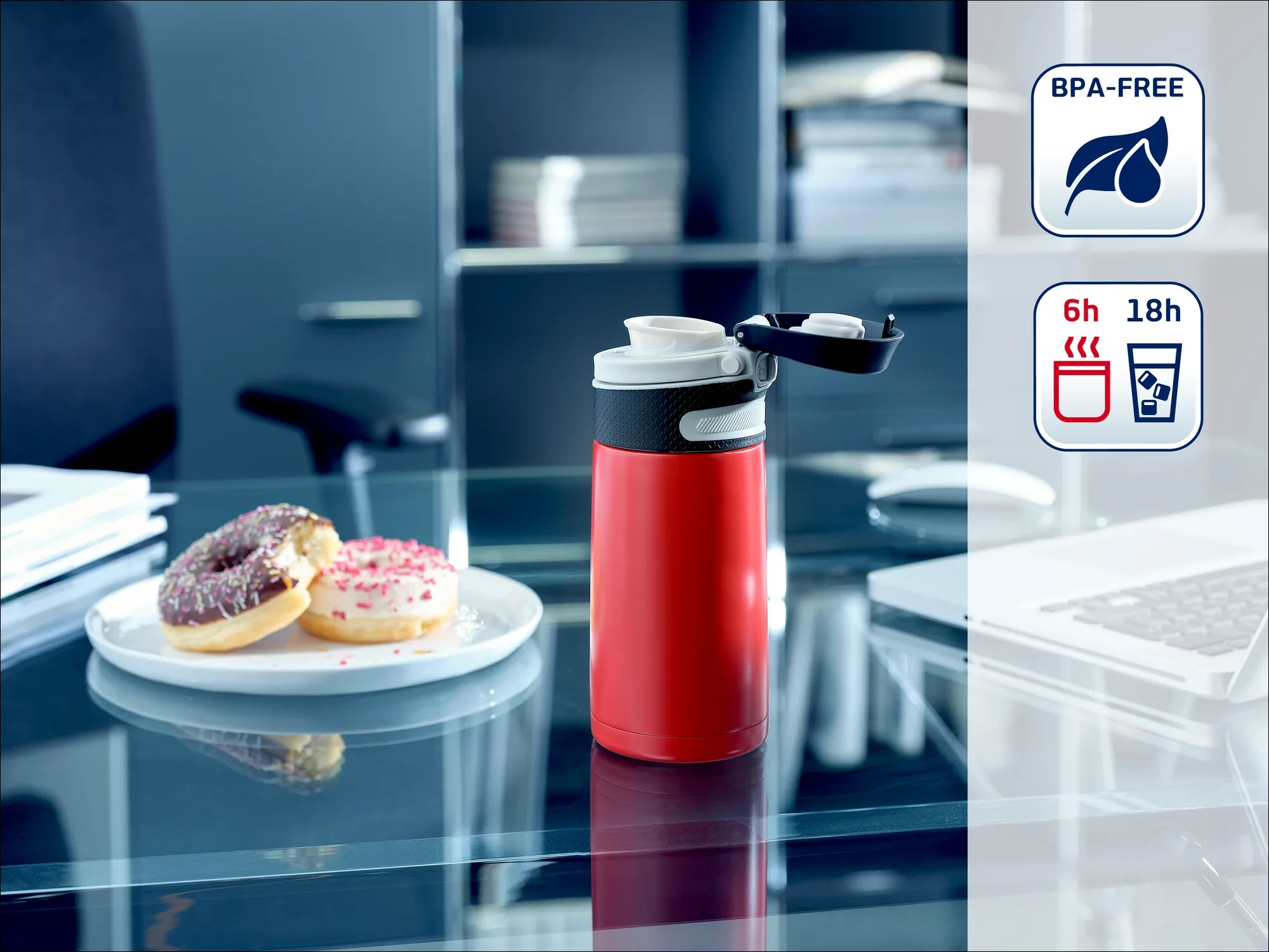 Czerwony termos na biurku z otwartą pokrywką, obok talerz z pączkami. W tle półka biurowa. Nie zawiera BPA, utrzymuje temperaturę napojów przez 6 godzin, a zimno przez 18 godzin.