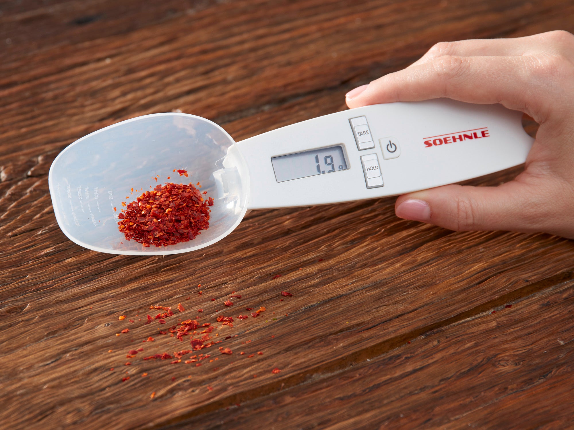 Eine Hand hält die digitale Küchenwaage Cooking Star von Soehnle. Die Waage zeigt 1,9 Gramm an und wiegt rote Gewürze auf einem Holzuntergrund. Ideal für präzises Abmessen.
