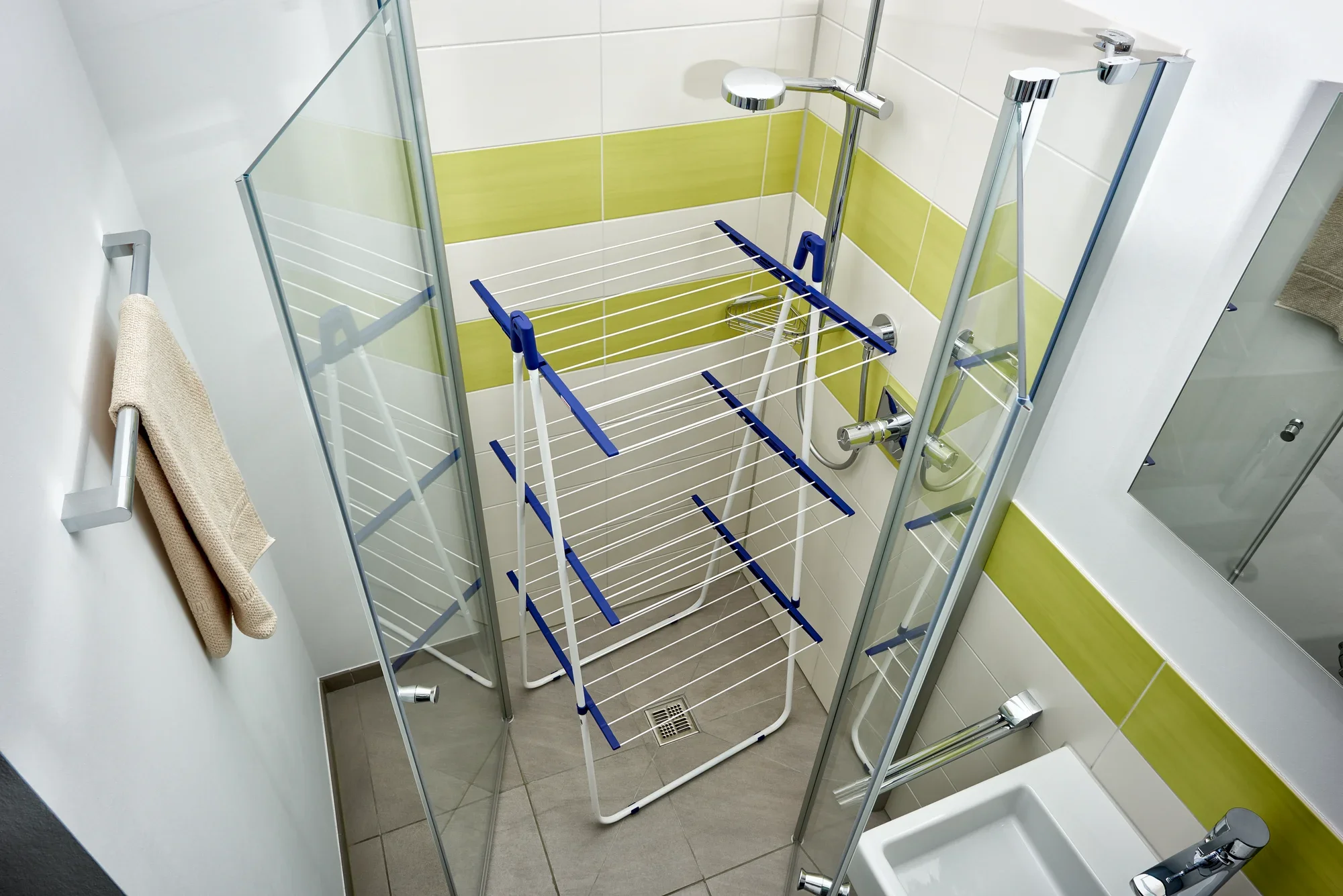 Een Pegasus Tower 190 droogtoren staat in een moderne douche met glazen wanden. De droger heeft verschillende niveaus om kleding op te hangen en is ontworpen om ruimte te besparen.