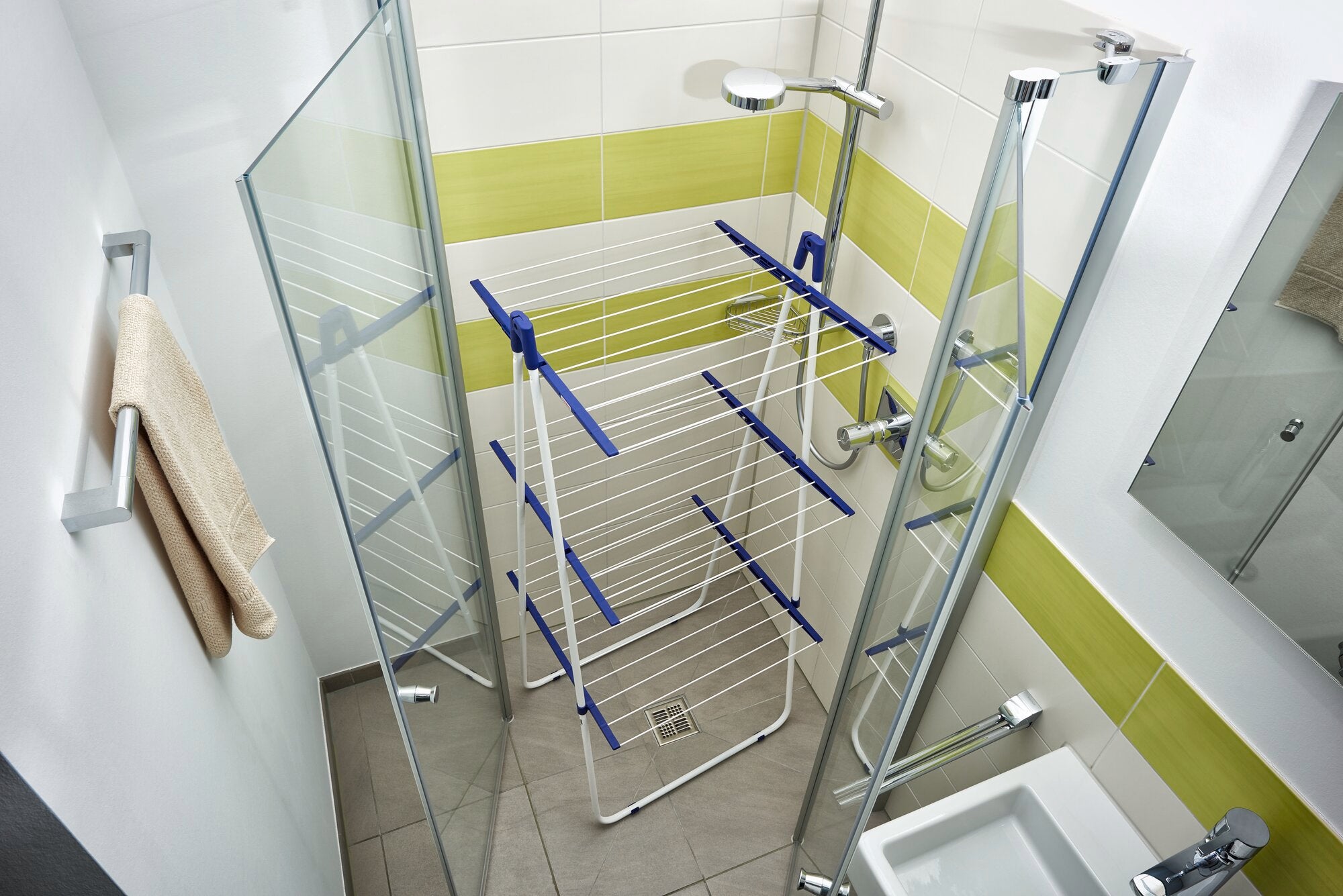 Een Pegasus Tower 190 droogtoren staat in een moderne douche met glazen wanden. De droger heeft verschillende niveaus om kleding op te hangen en is ontworpen om ruimte te besparen.