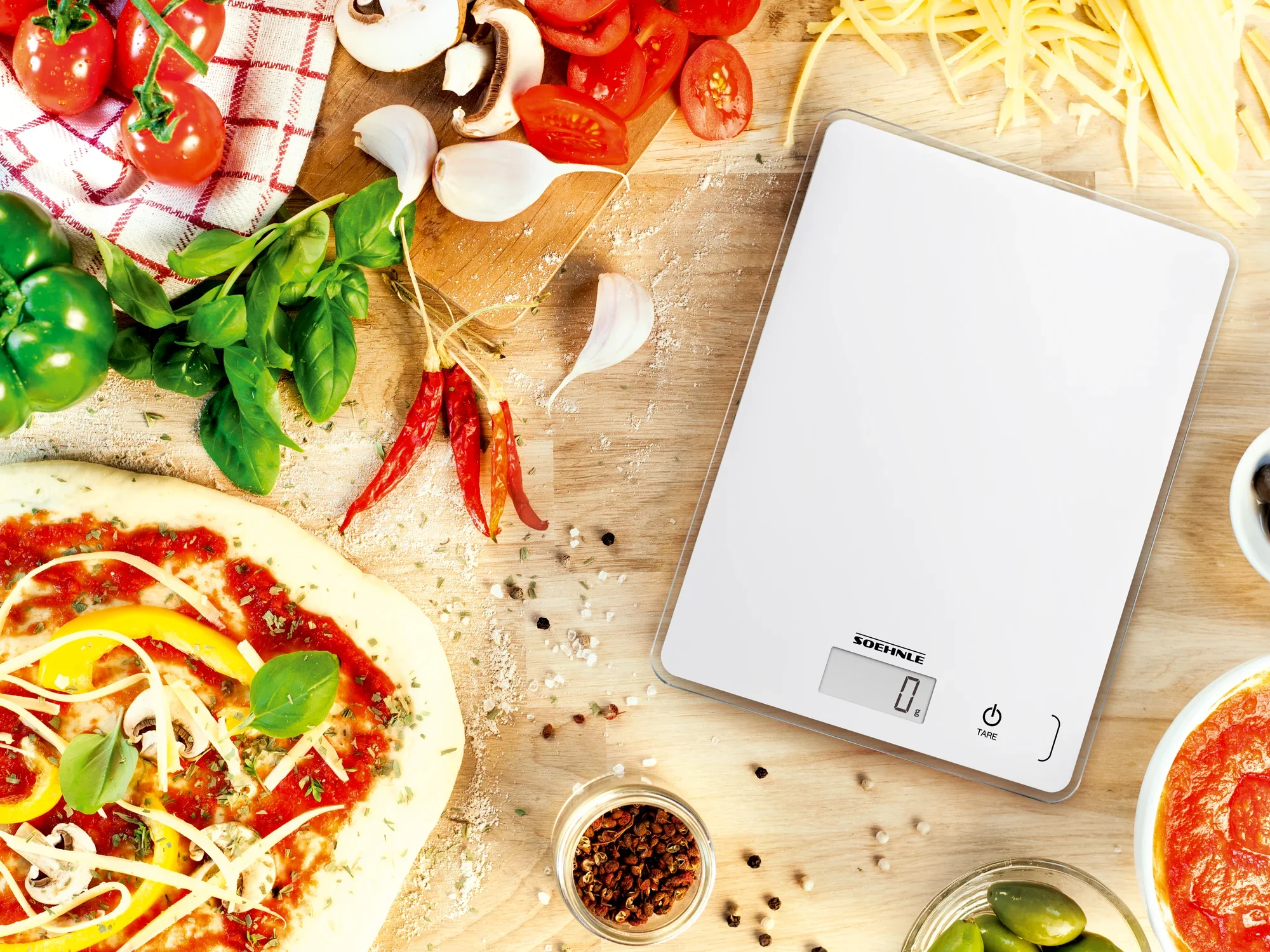 Page Compact 300 digital kitchen scales on a wooden table surrounded by fresh ingredients such as tomatoes, basil and peppers. Perfect for precise cooking and baking.