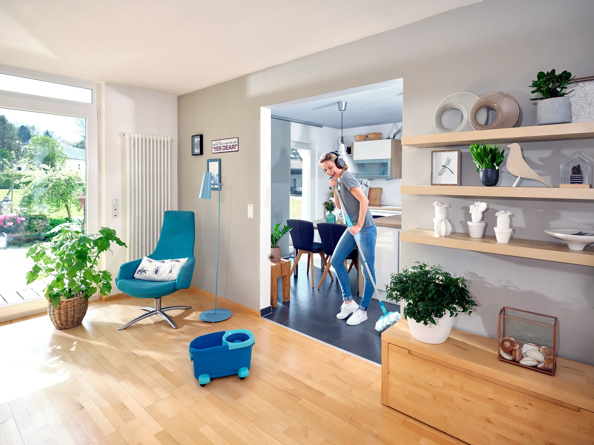 Una donna pulisce il pavimento di un soggiorno moderno con il CLEAN TWIST Disc Mop Ergo. La stanza è luminosa e arredata con stile, con piante e decorazioni.