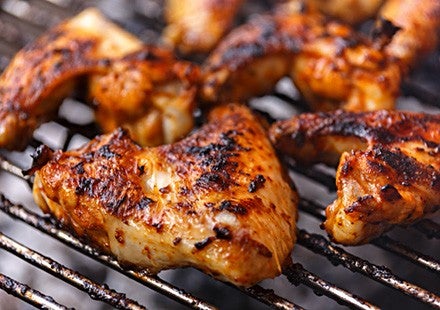 Gegrillte Haehnchenfluegel mit knuspriger, brauner Haut und Gewuerzen auf einem Grillrost.