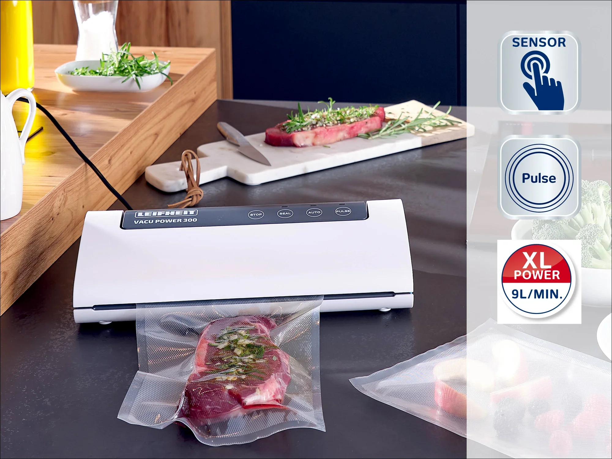 Machine sous vide Leifheit : une machine sous vide blanche posée sur un plan de travail de cuisine, en train de mettre de la viande sous vide. En arrière-plan, des herbes fraîches et de la viande. La fonction capteur et la fonction pulse sont mises en ava