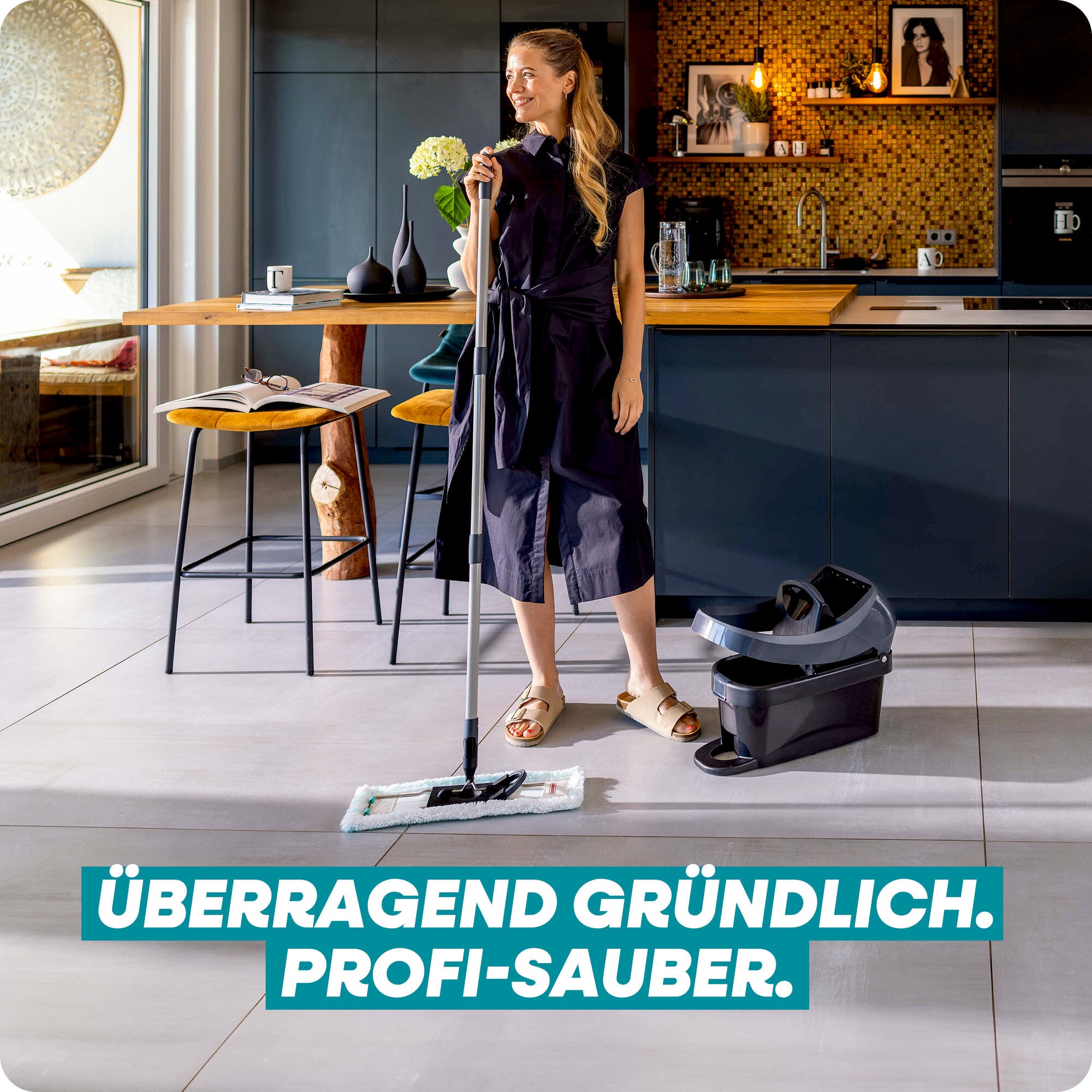 Leifheit Set Profi XL Mobile Black: Eine Frau wischt in einer modernen Küche mit dem Bodenwischer über helle Fliesen; daneben steht der mobile Eimer mit Pressaufsatz für gründliche, komfortable Bodenreinigung.