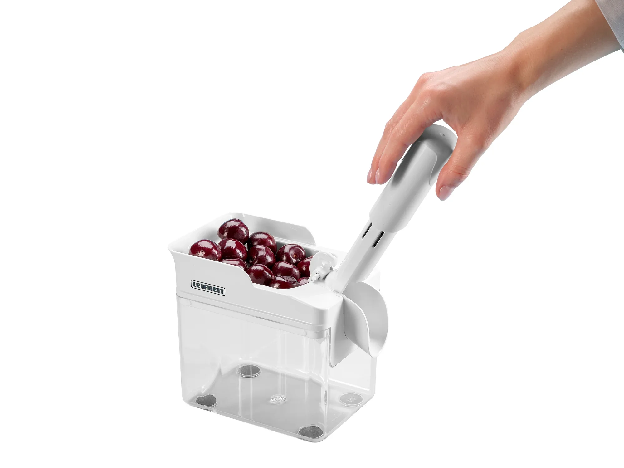 Kirschentkerner Cherrymat in Aktion: Eine Hand bedient den weißen Kirschentkerner, der Kirschen in einem transparenten Behälter entkernt. Ideal für schnelles und einfaches Entkernen.