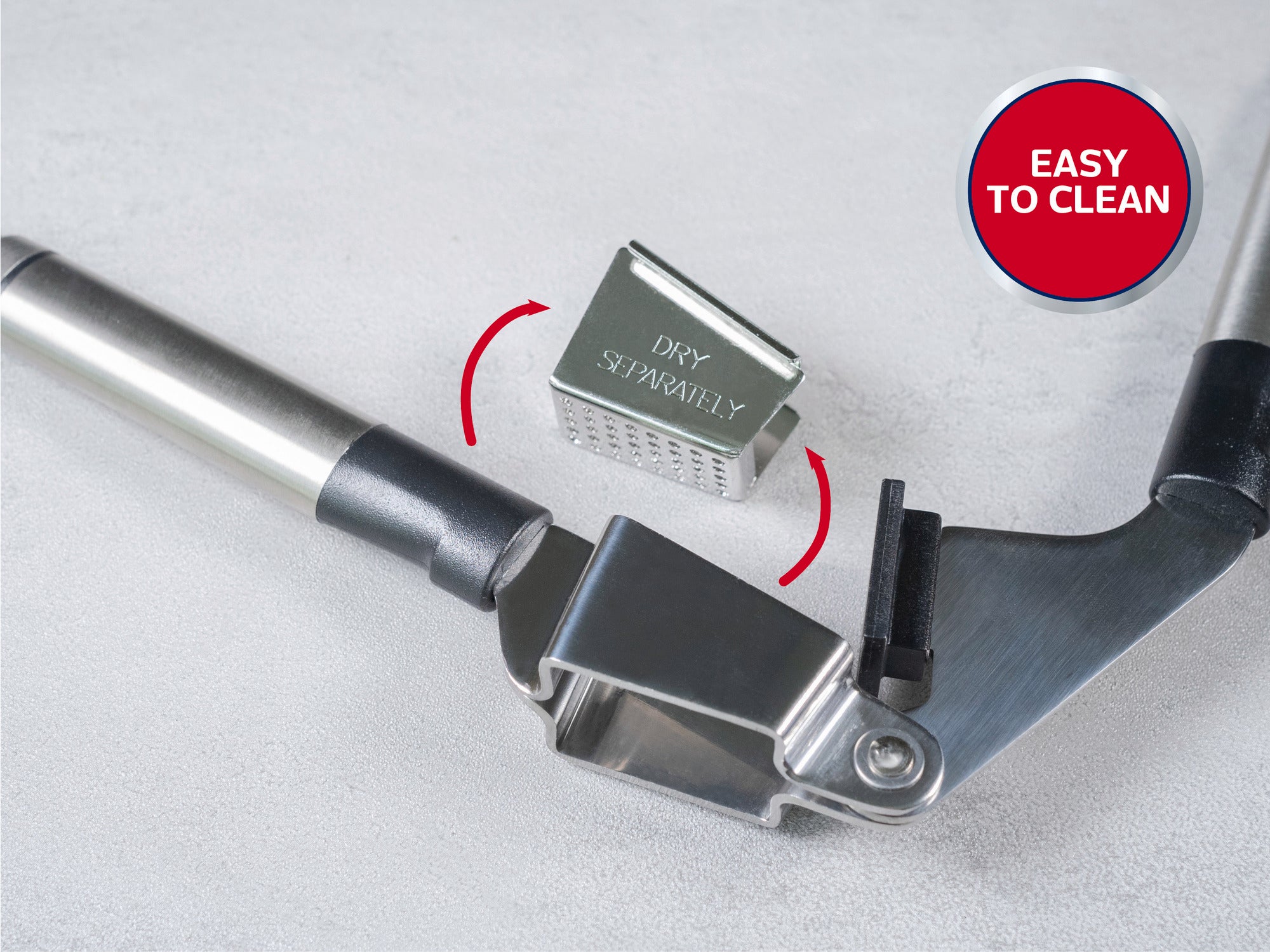 Presse-ail inoxydable avec insert amovible et etiquettes "Dry Separately" et "Easy to Clean", sur fond gris clair.