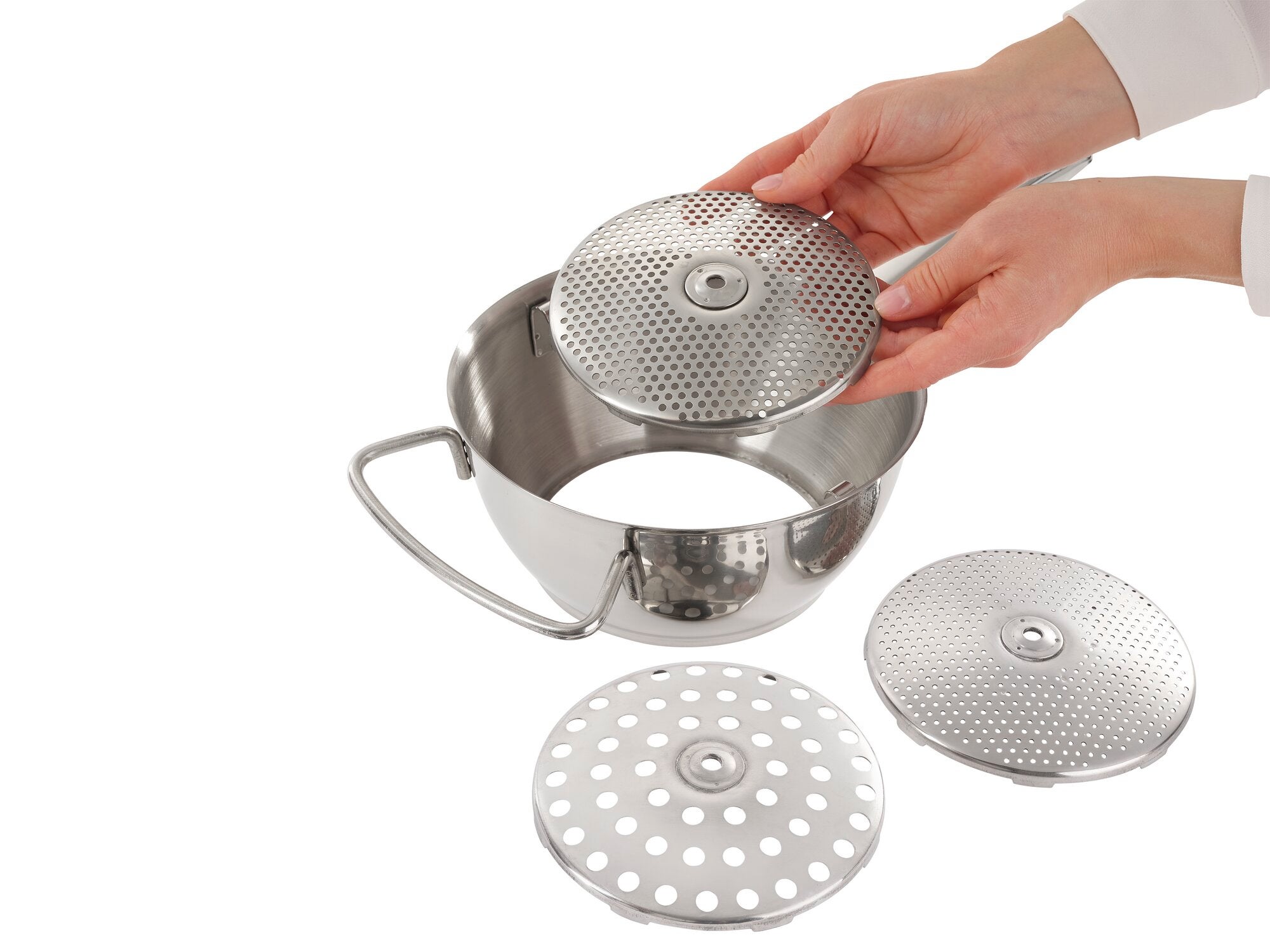 Stainless steel food mill with three interchangeable discs. Two hands show how to insert a disc into the mill. Ideal for puréeing fruit and vegetables.