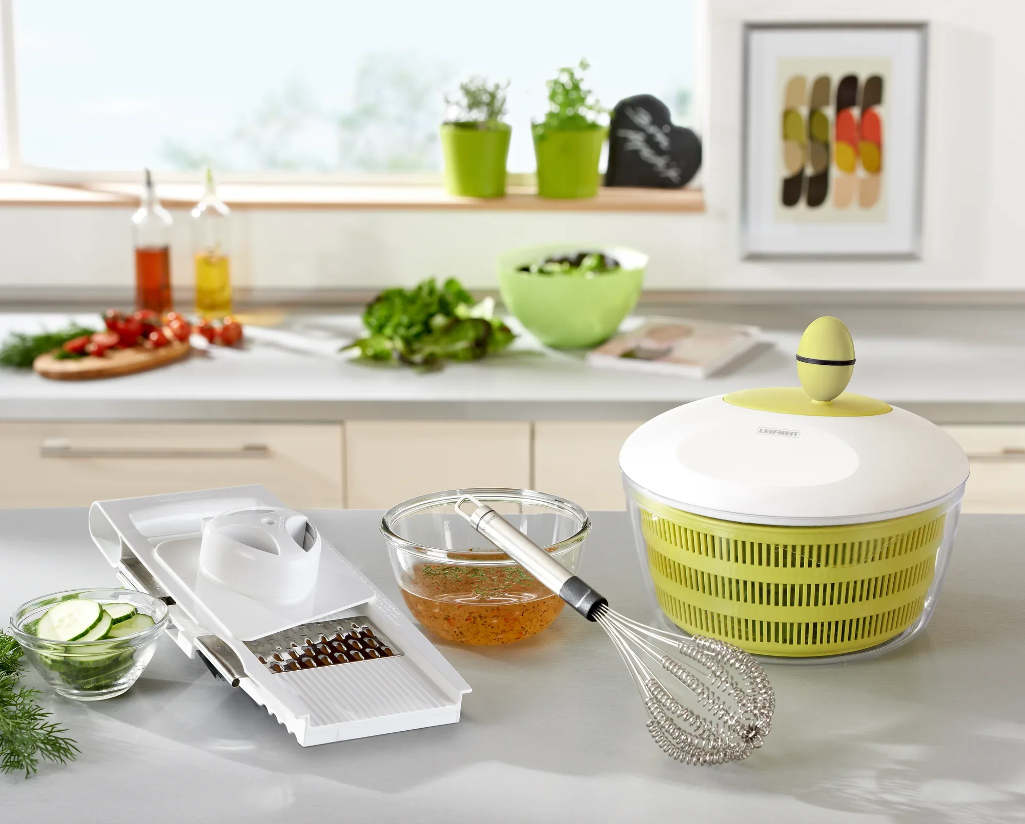 Salaterka Trend w nowoczesnej kuchni. Wirówka do sałatek stoi na blacie obok trzepaczki, tarki i miski. W tle widać zioła i przyprawy.