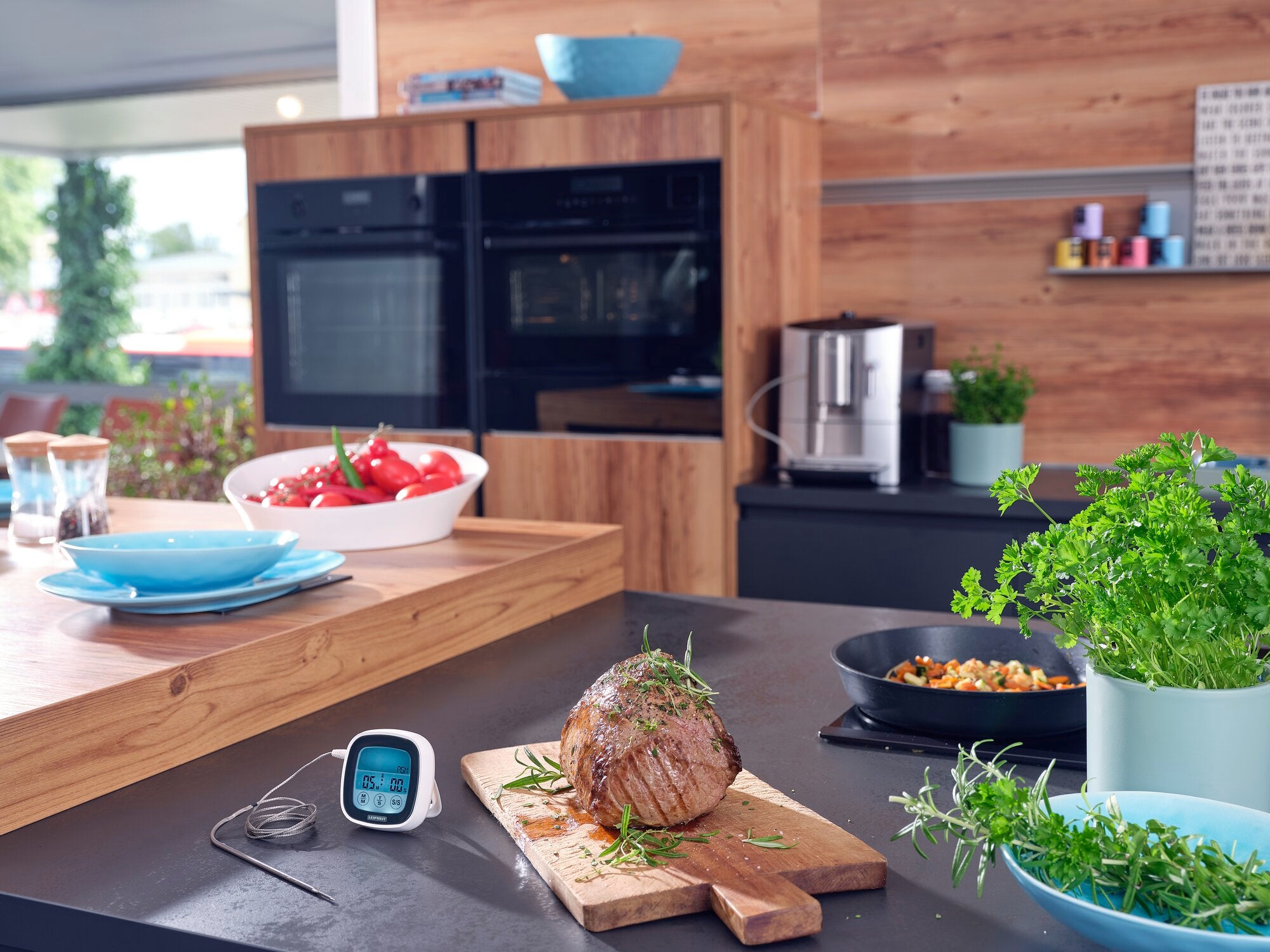 Een moderne braad- en BBQ-thermometer ligt op een keukenblad naast een sappig braadstuk. Op de achtergrond zie je een oven en verse kruiden.