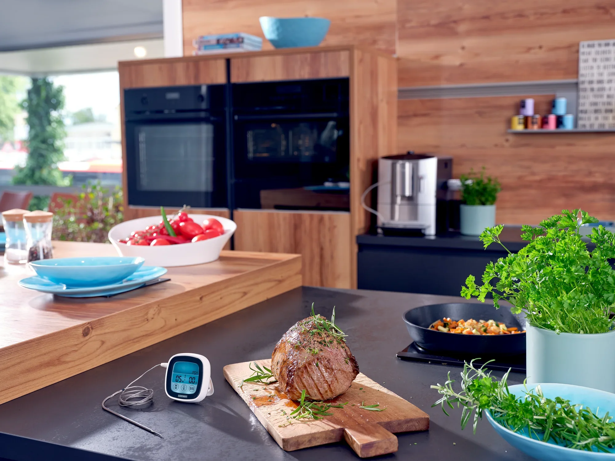 Nowoczesny termometr do pieczenia i grillowania leży na blacie kuchennym obok soczystej pieczeni. W tle widać piekarnik i świeże zioła.