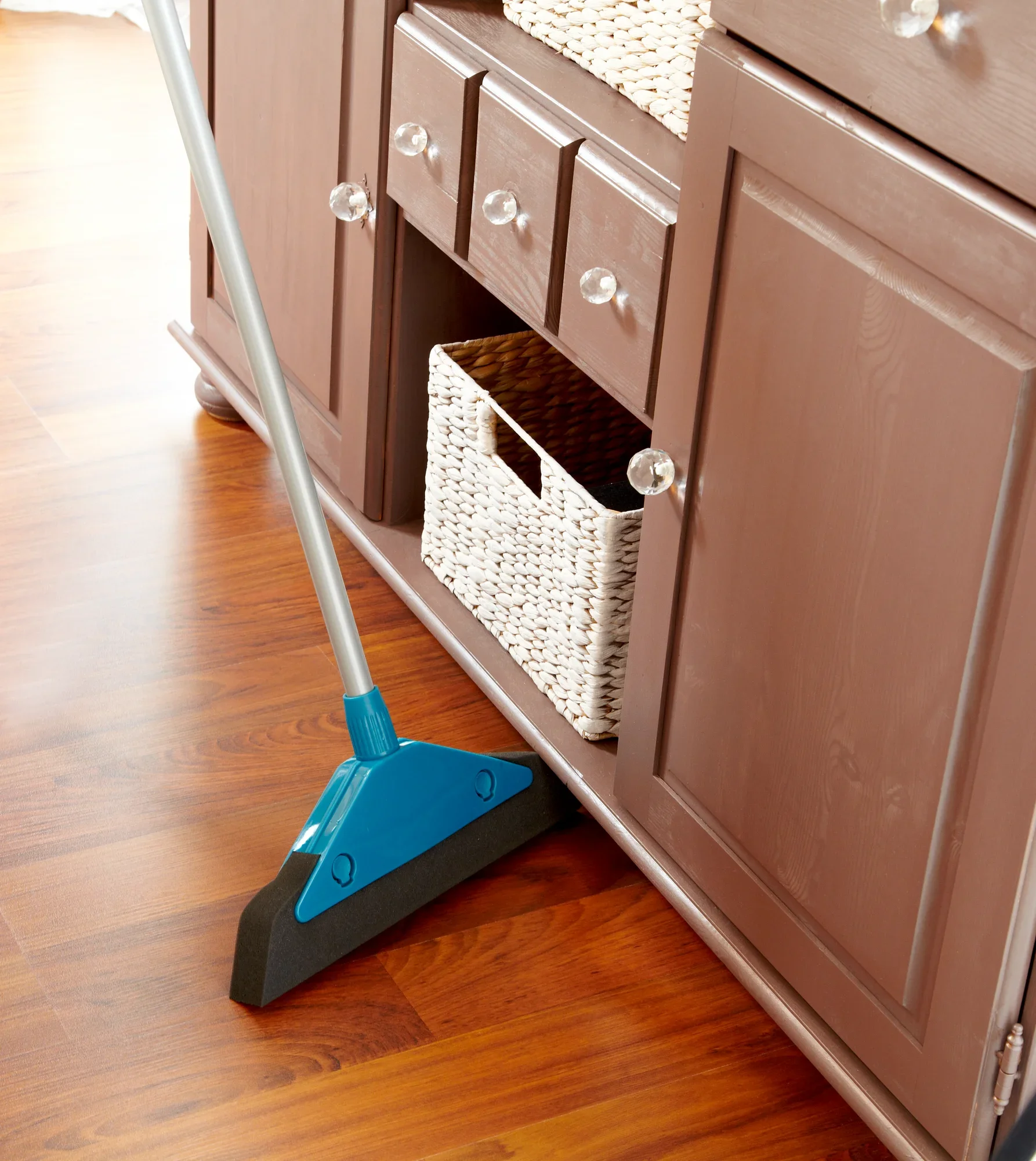 Un balai en mousse avec un manche bleu est utilisé pour enlever la poussière et la saleté d'un parquet. Le balai est idéal pour les surfaces délicates et atteint facilement les coins.
