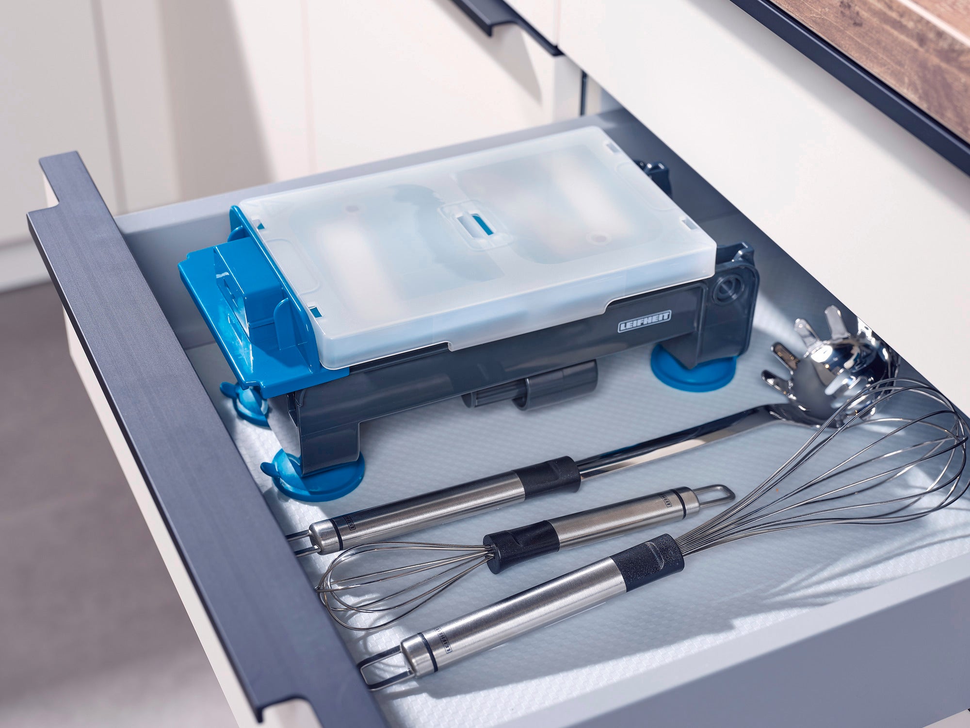 A table-top spiral slicer is neatly stored in a kitchen drawer next to a whisk and other kitchen utensils. The spiral slicer is compact and space-saving.