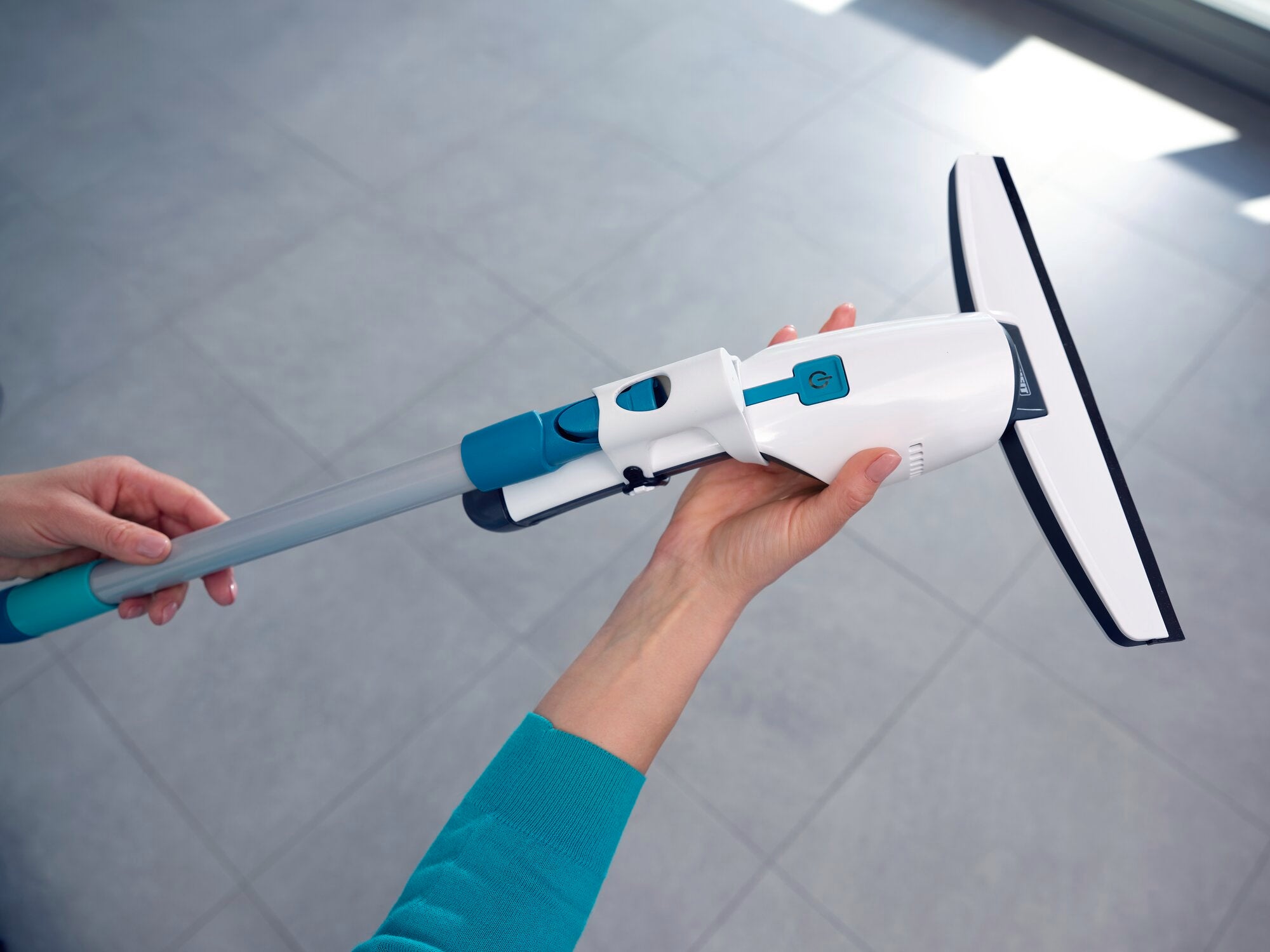 A Nemo window vacuum cleaner is held in one hand. The vacuum cleaner has a modern design with blue and white elements and is ideal for cleaning windows and smooth surfaces.
