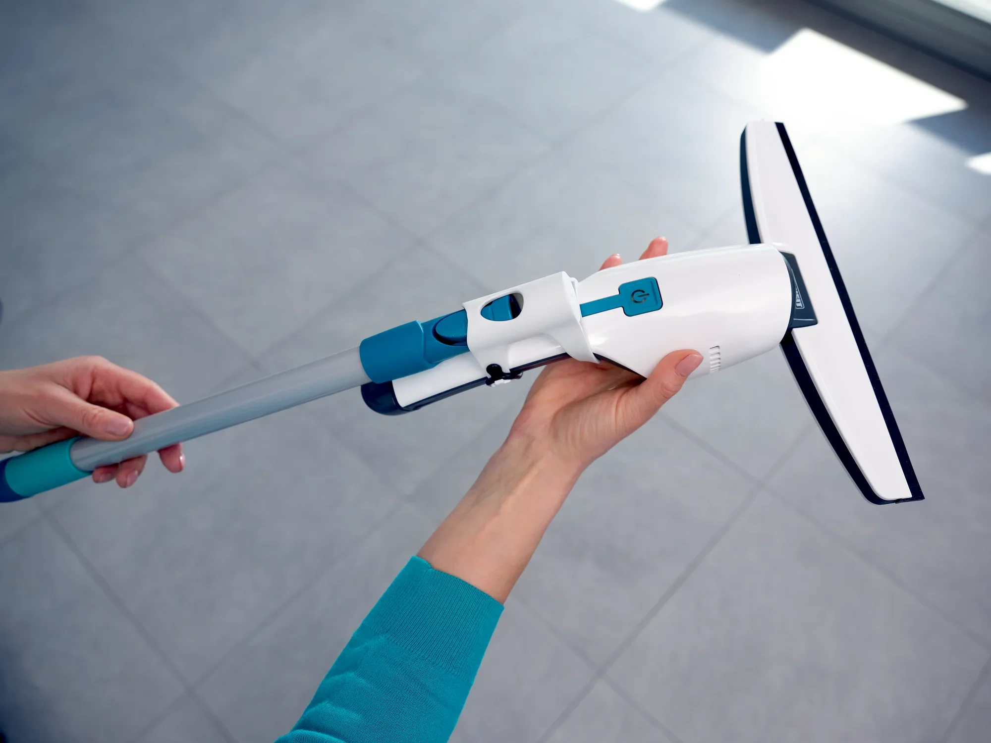 Odkurzacz do okien Nemo jest trzymany w jednej ręce. Odkurzacz ma nowoczesny design z niebieskimi i białymi elementami i jest idealny do czyszczenia okien i gładkich powierzchni.