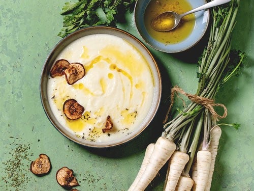 Cremige Pastinakensuppe, garniert mit Pilzen und Kraeutern, daneben frische Pastinaken und eine Schale mit