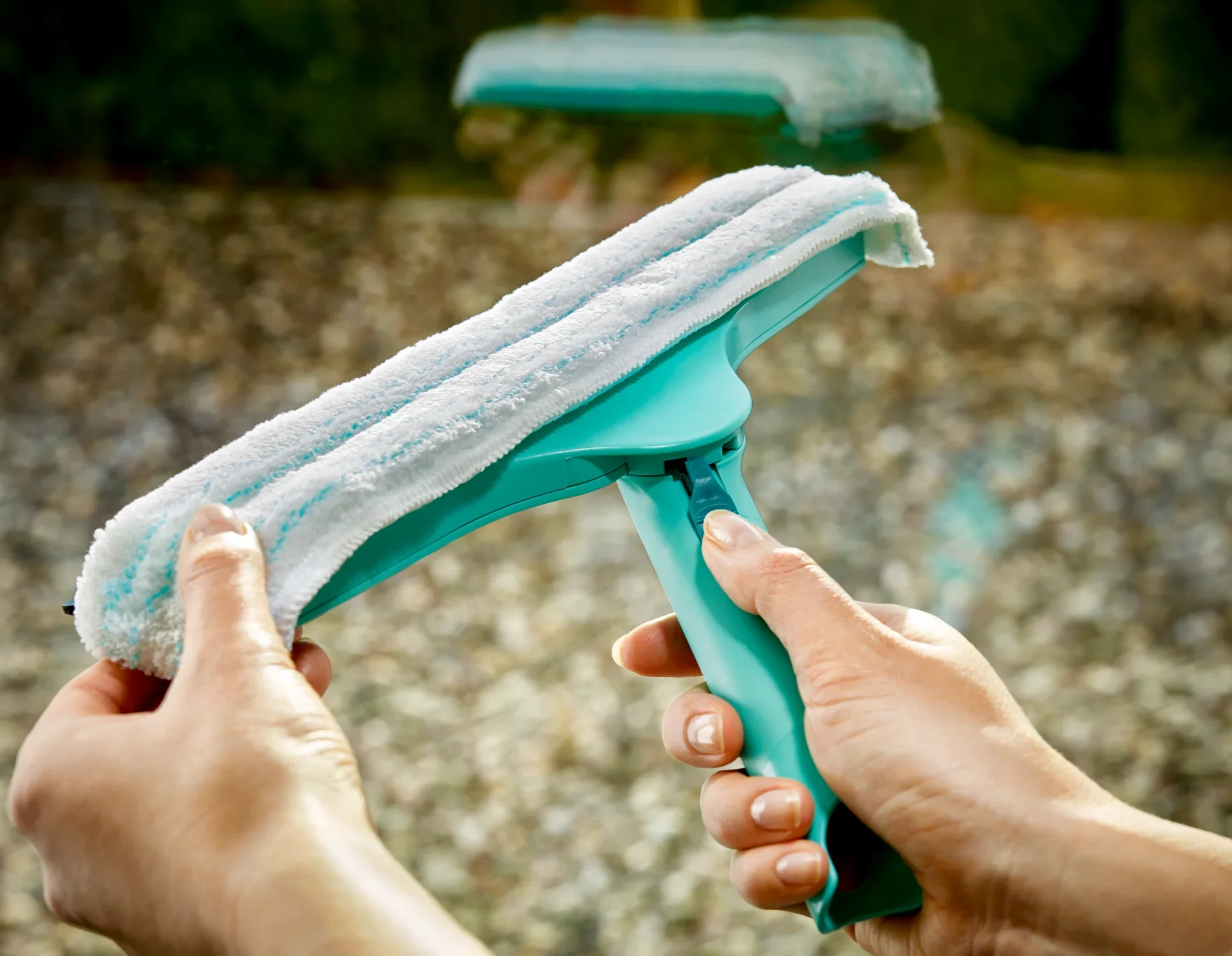 Tergivetro 3in1 in azione. Una persona tiene il tergivetro turchese con un panno in microfibra bianco mentre pulisce una finestra. Ideale per una pulizia senza aloni.