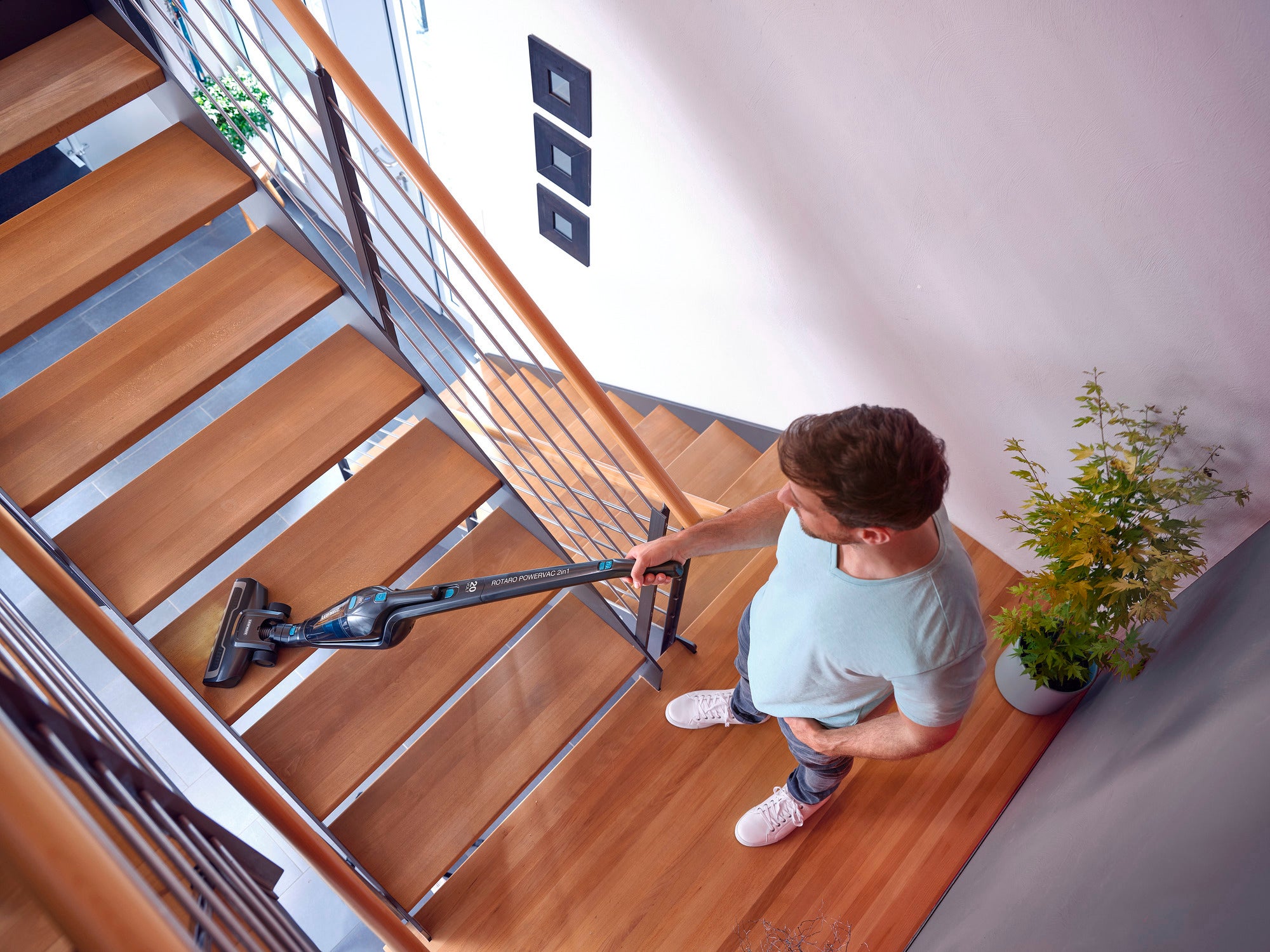 Ein Mann benutzt den Akku-Staubsauger Rotaro PowerVac, um eine Holztreppe zu reinigen. Der Staubsauger ist leicht und kabellos, ideal für schwer zugängliche Stellen.