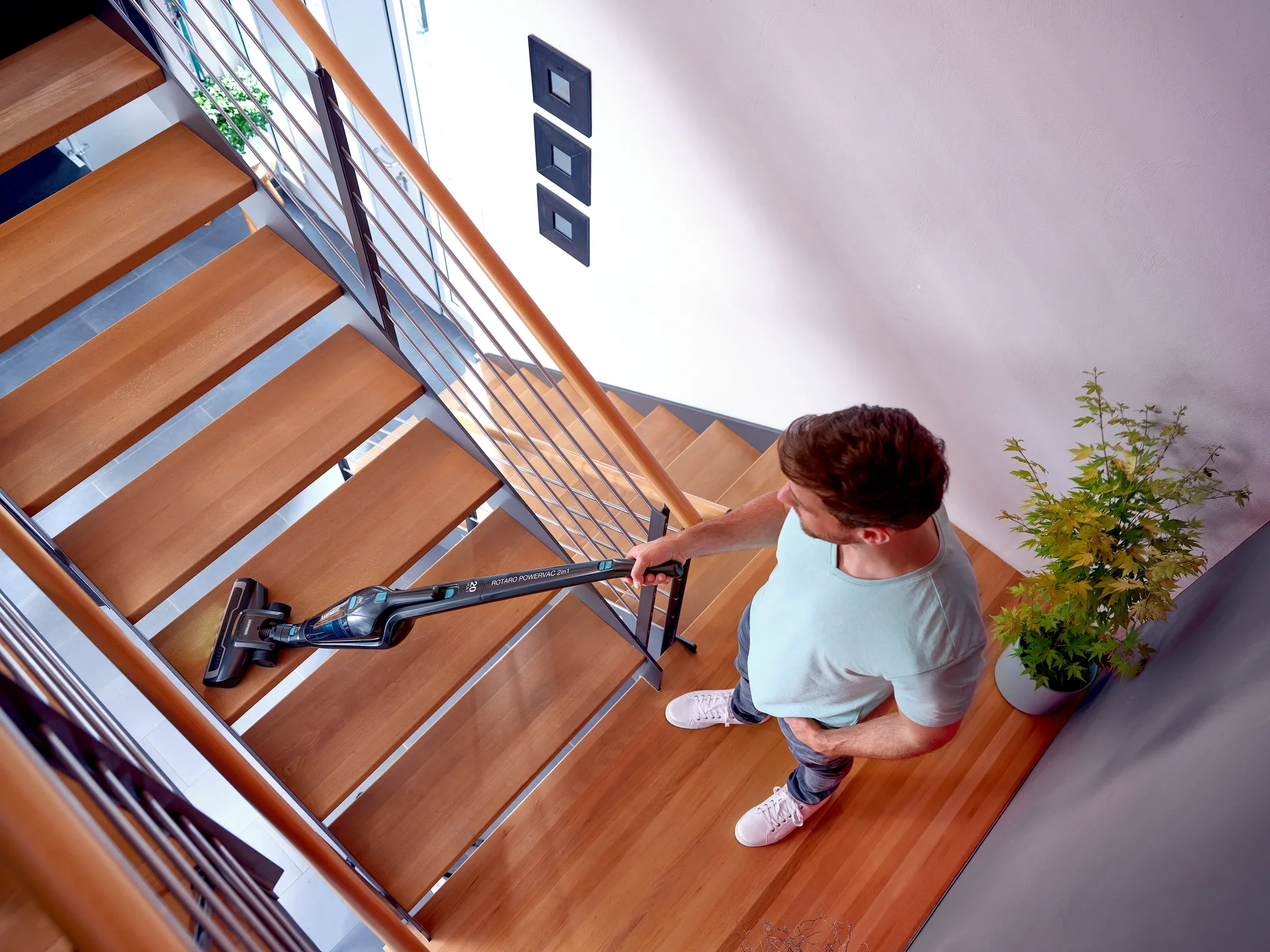 Un homme utilise l'aspirateur sans fil Rotaro PowerVac pour nettoyer un escalier en bois. L'aspirateur est léger et sans fil, idéal pour les endroits difficiles d'accès.