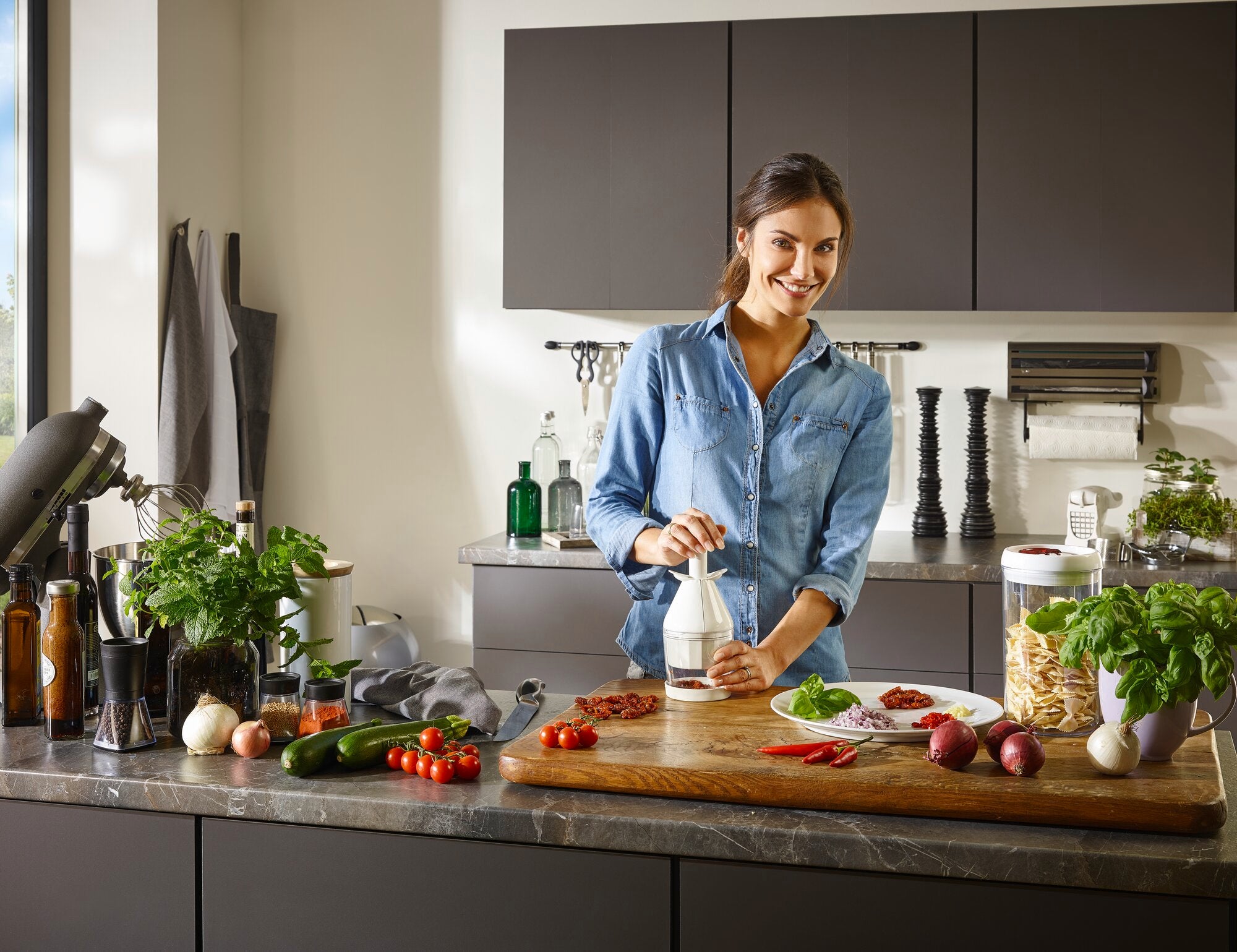Vrouw in een moderne keuken gebruikt een uien- en groentensnijder. Verse ingrediënten zoals tomaten, uien en kruiden worden op het werkblad gelegd. Ideaal om snel en efficiënt te koken.