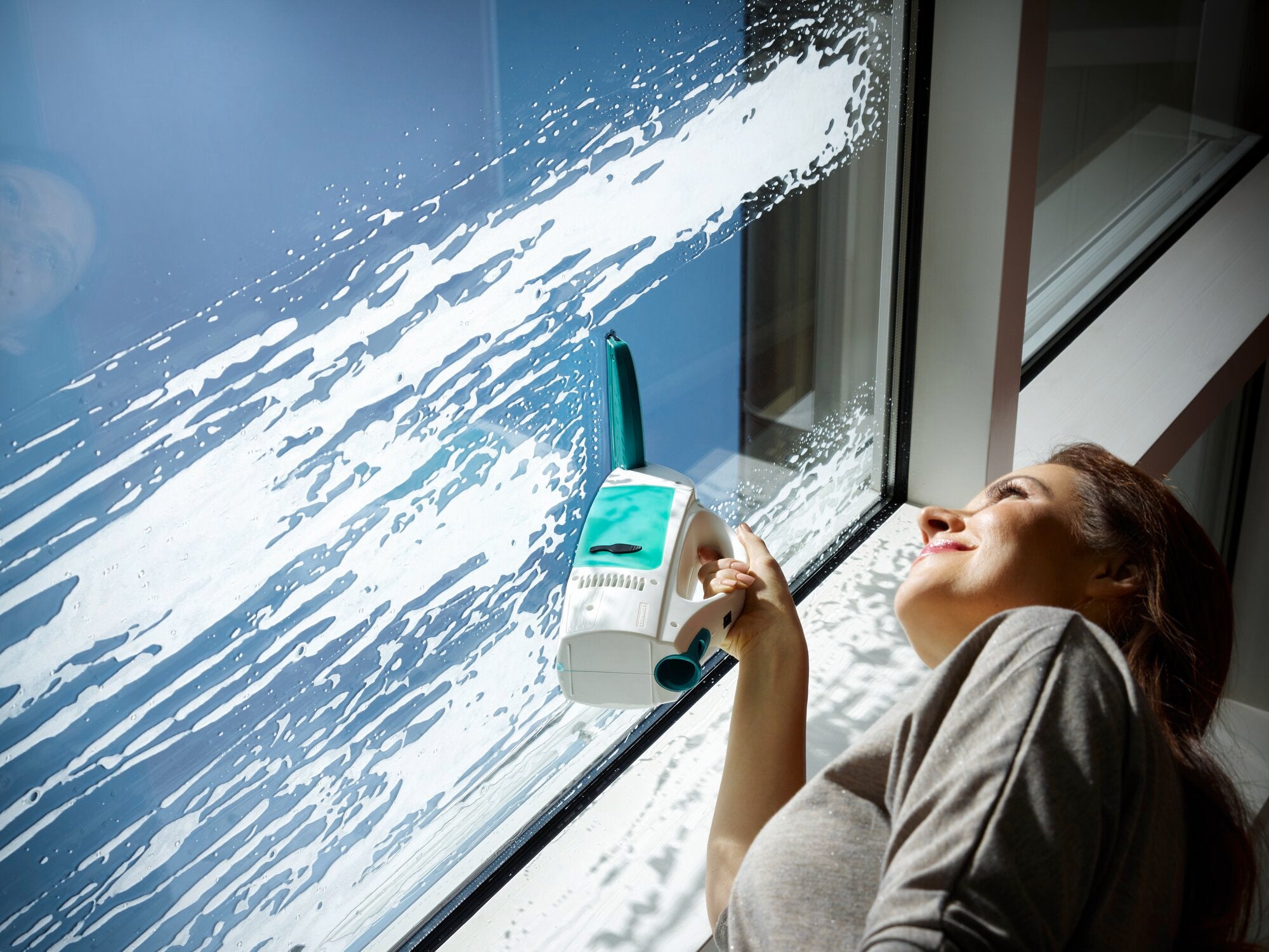 Eine Frau reinigt ein großes Fenster mit dem Fenstersauger Dry and Clean. Der Sauger entfernt effizient Wasser und Schmutz, während die Frau zufrieden lächelt.