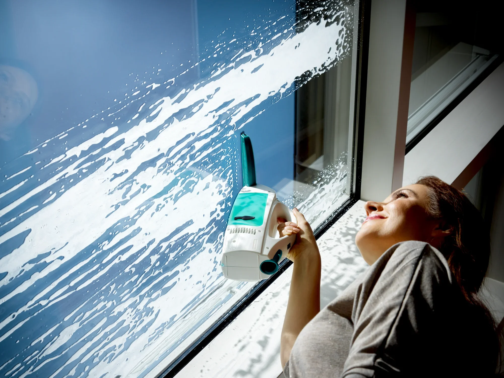 Kobieta czyści duże okno za pomocą odkurzacza do okien Dry and Clean. Odkurzacz skutecznie usuwa wodę i brud, a kobieta uśmiecha się z zadowoleniem.