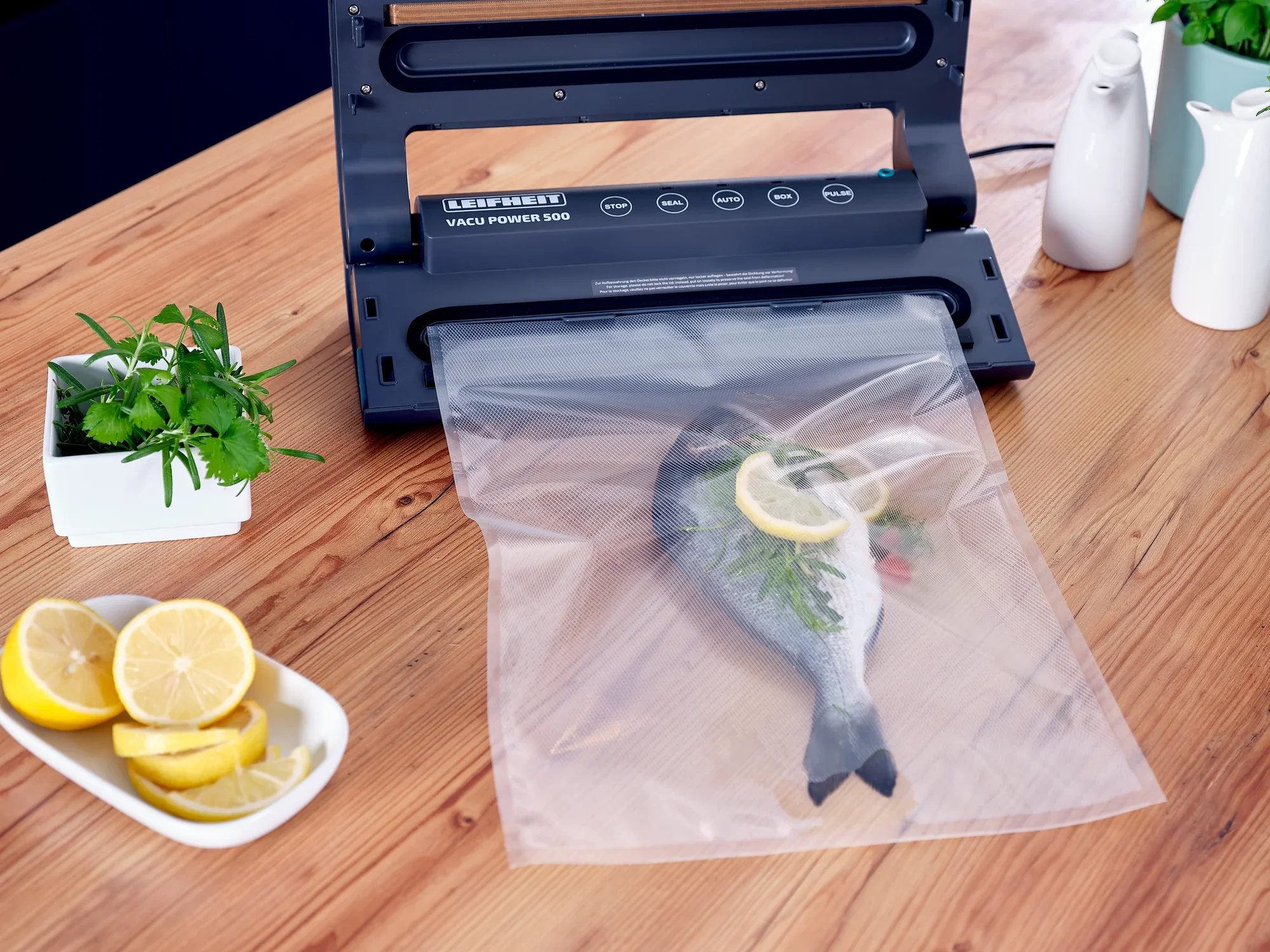 Sacchetti sottovuoto 30x40 cm: una macchina sottovuoto chiude un sacchetto con un pesce, guarnito con una fetta di limone ed erbe aromatiche. Accanto ci sono fette di limone ed erbe aromatiche fresche.