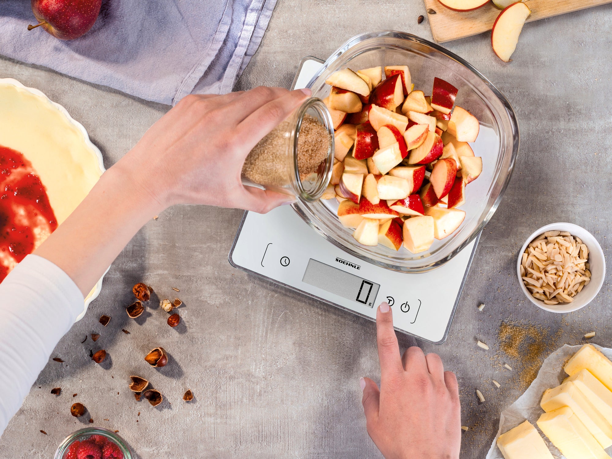 Een persoon weegt gesneden appels in een kom op de Page Comfort 400 digitale keukenweegschaal. De weegschaal toont het gewicht terwijl ingrediënten worden bereid.