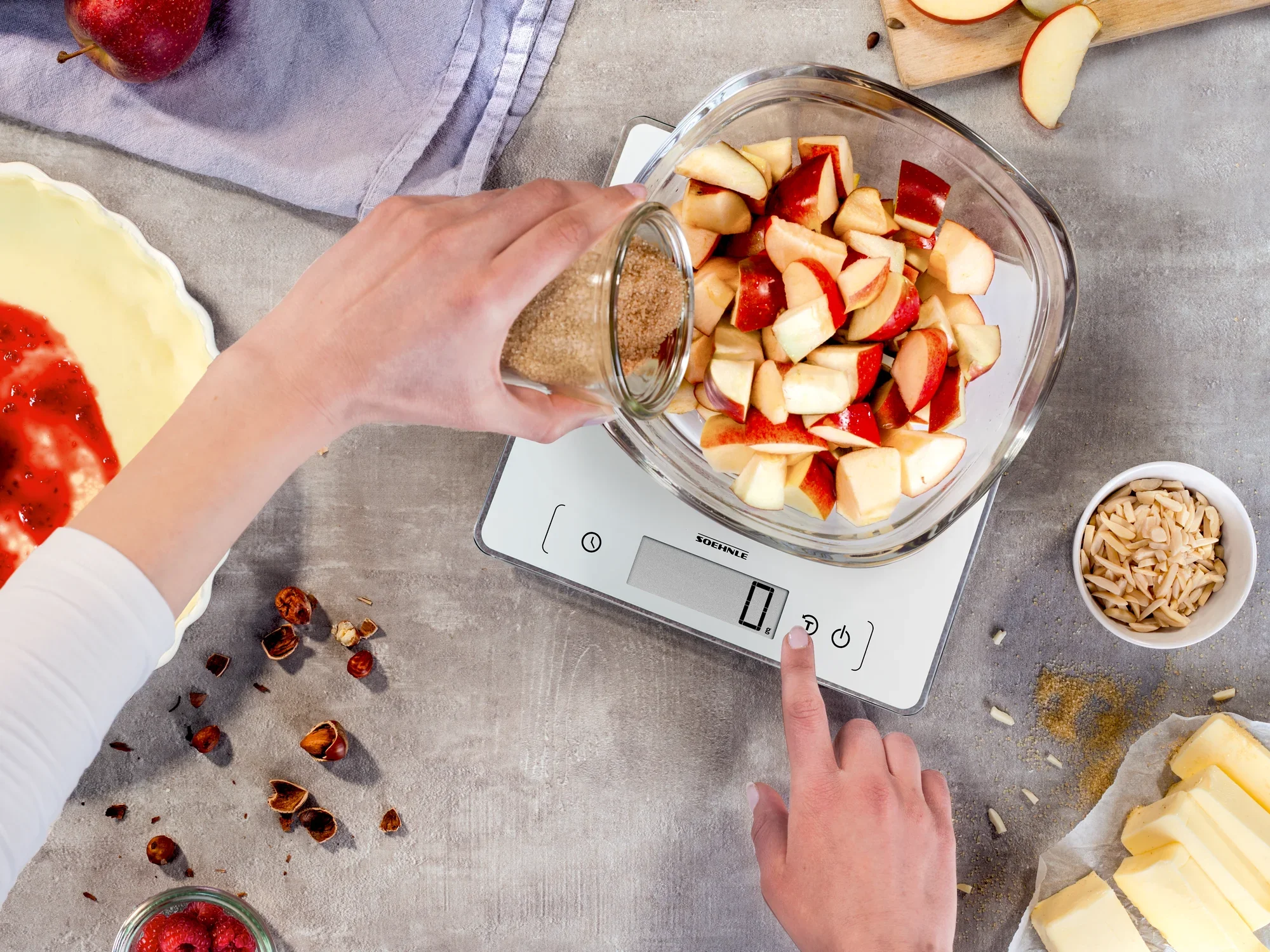 Eine Person wiegt geschnittene Äpfel in einer Schüssel auf der digitalen Küchenwaage Page Comfort 400. Die Waage zeigt das Gewicht an, während Zutaten vorbereitet werden.
