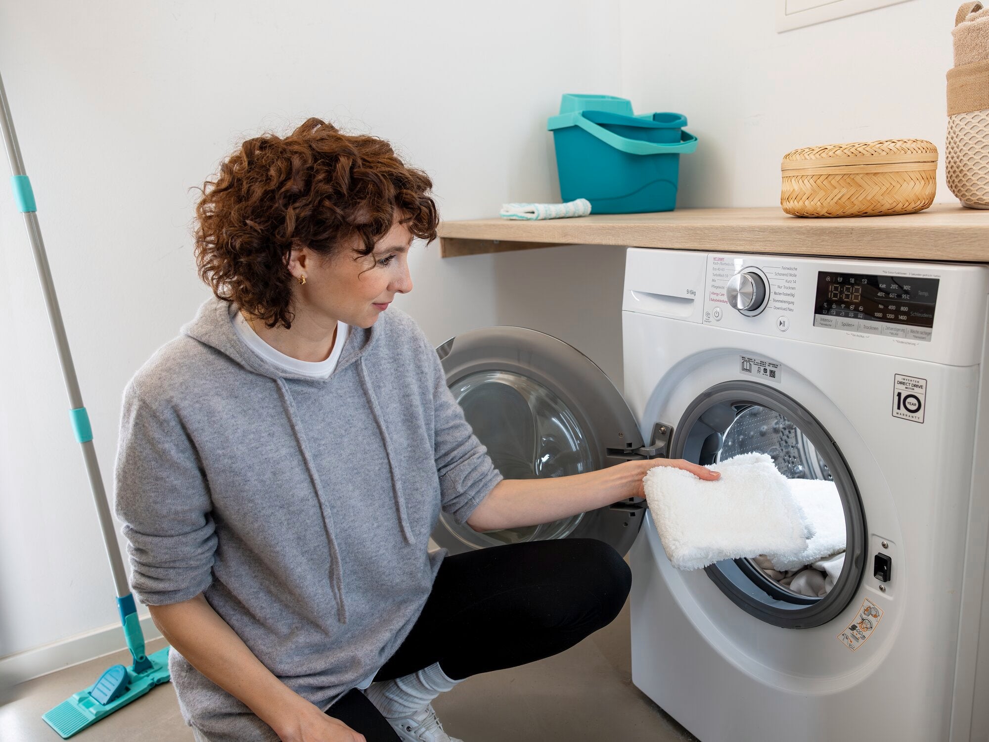 Een vrouw knielt voor een wasmachine en plaatst de SUPERDUSTER stofmop erin, die wordt gebruikt om de vloer schoon te maken.