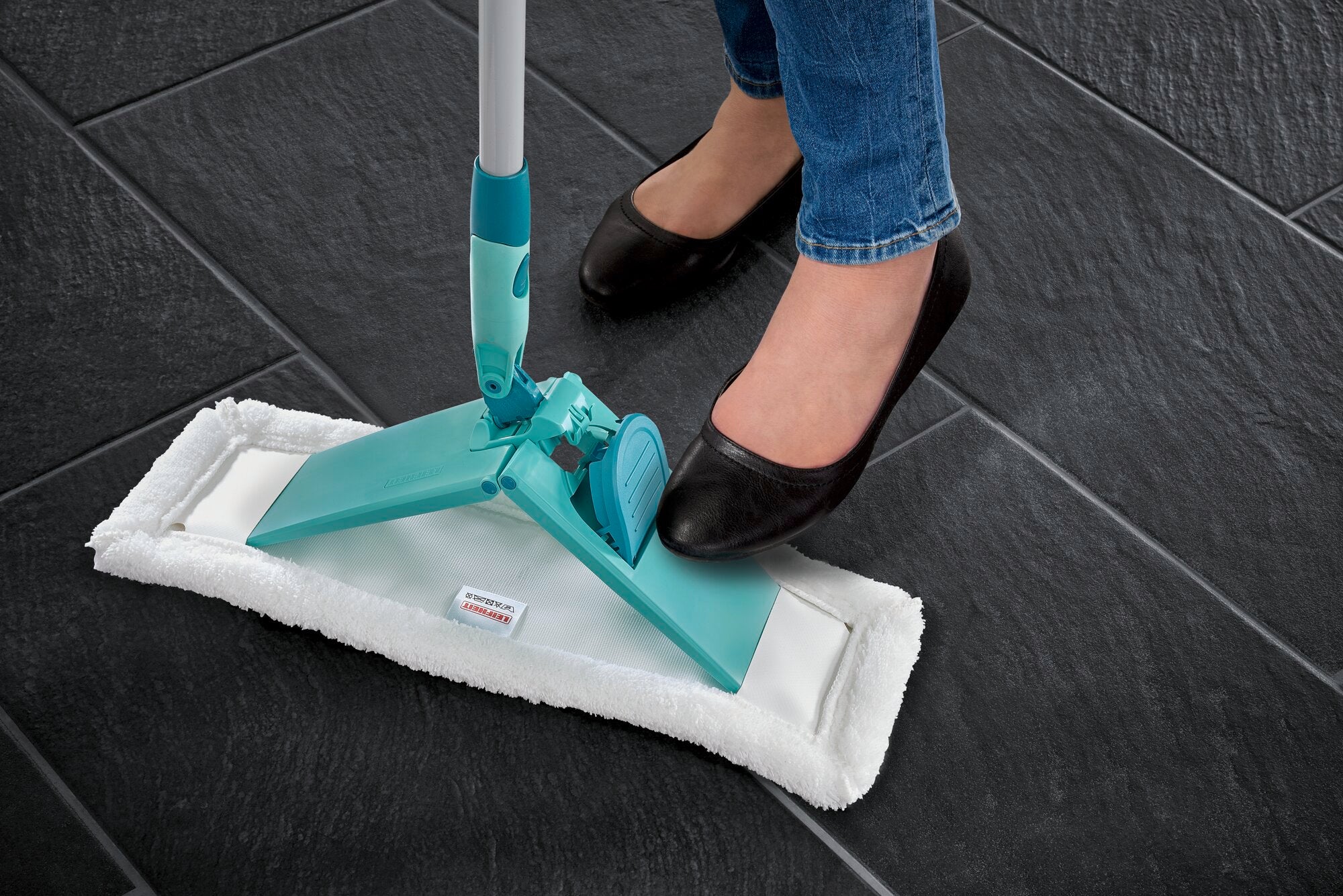 Bodenwischer Profi XL in Anwendung auf dunklem Fliesenboden. Eine Person mit schwarzen Schuhen betätigt den Fußmechanismus des Wischers, um den Bezug zu wechseln.