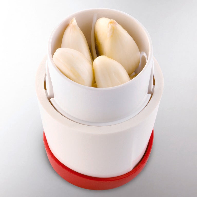 Quatre gousses d'ail pelees dans un presse-ail blanc et rouge sur fond gris clair.