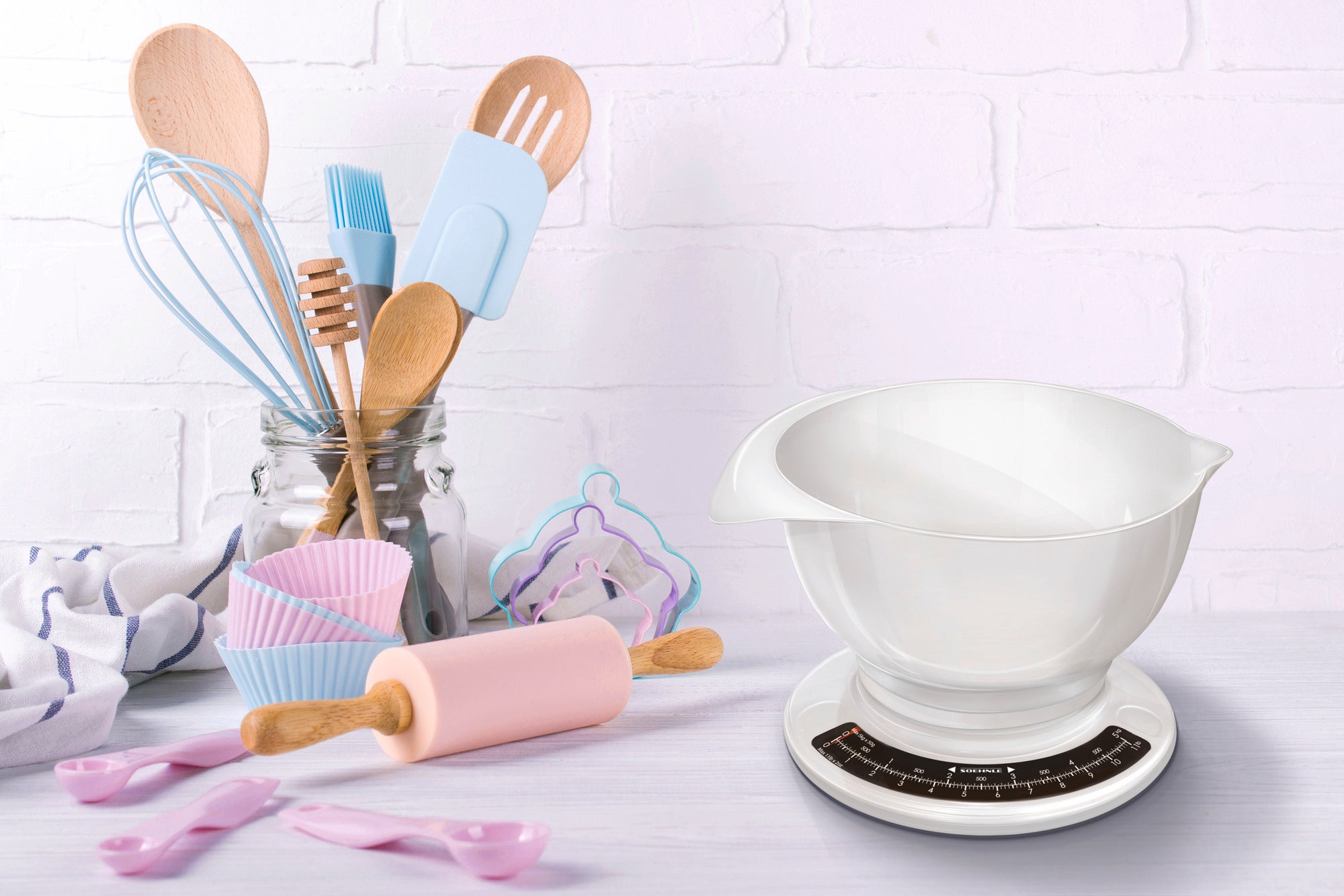 Eine analoge Küchenwaage Culina Pro steht auf einer Arbeitsfläche. Daneben befinden sich bunte Küchenutensilien wie ein Nudelholz, Schneebesen und Messlöffel. Die Szene vermittelt eine einladende Backatmosphäre.