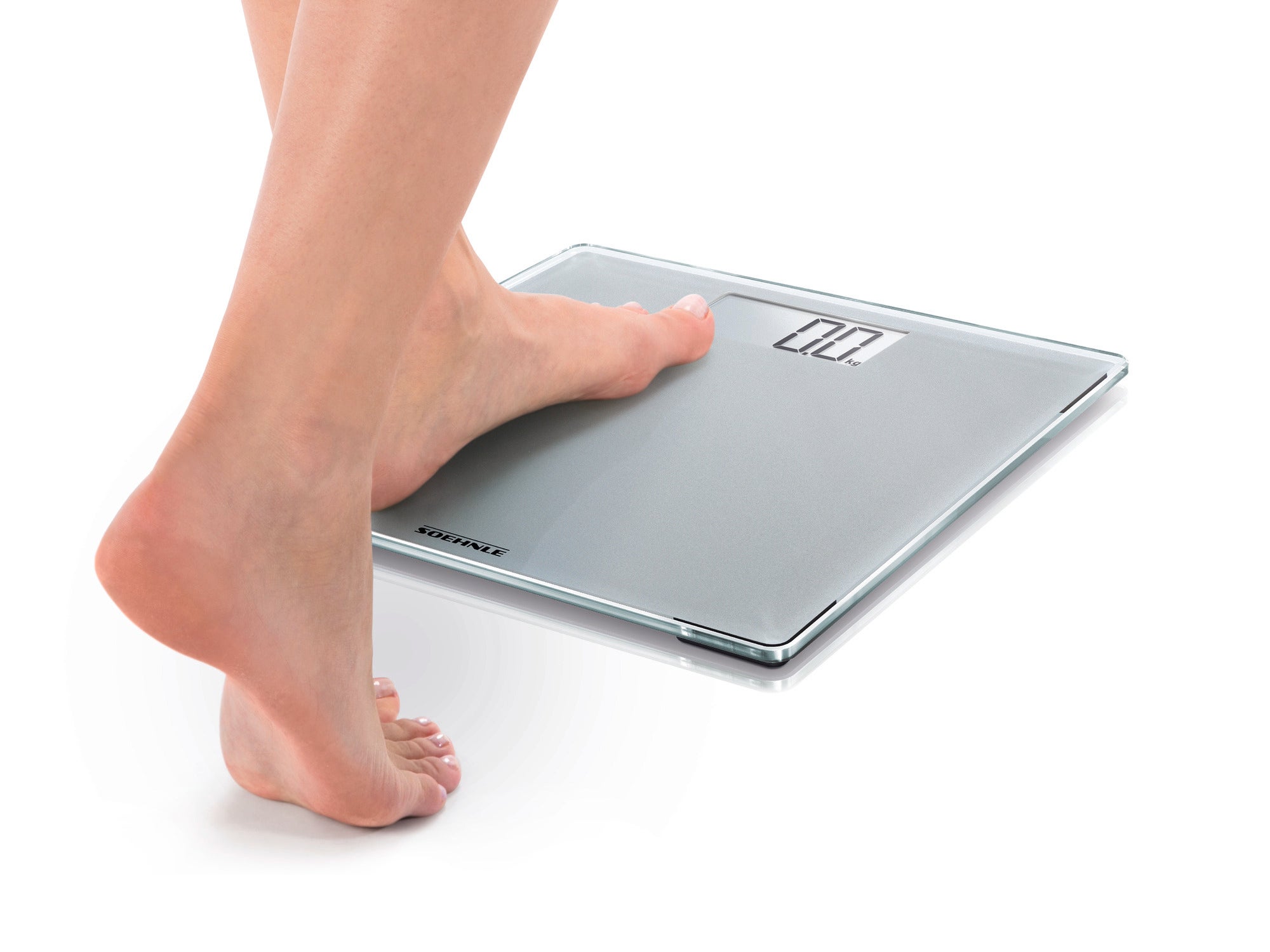 A person stands with one foot on the Style Sense Compact 300 digital bathroom scale. The scale has a modern, slim design and a clear display.