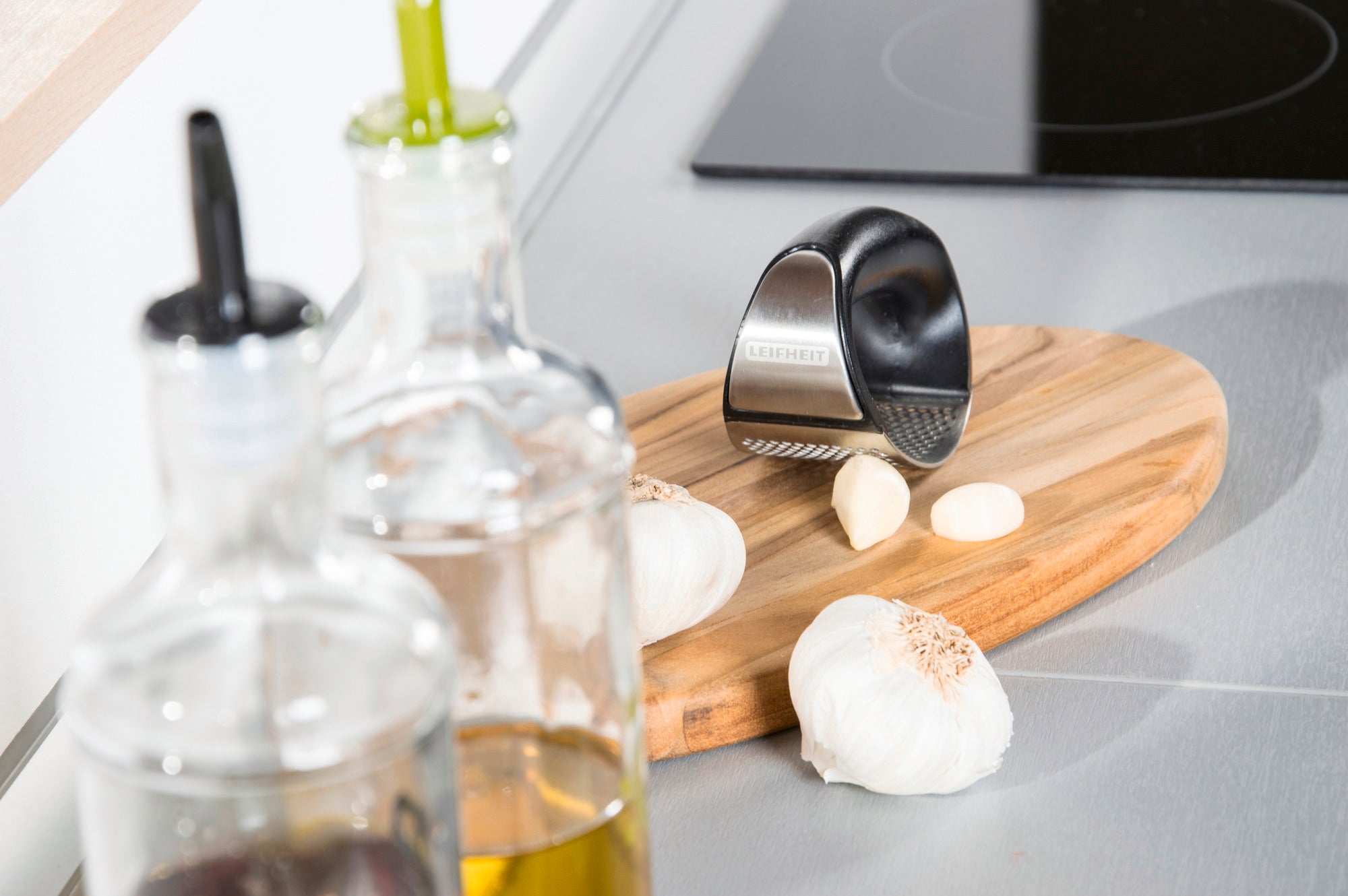 Knobi King garlic press on a wooden board in a modern kitchen. Garlic cloves and oil bottles can be seen in the foreground. Ideal for easily crushing garlic.