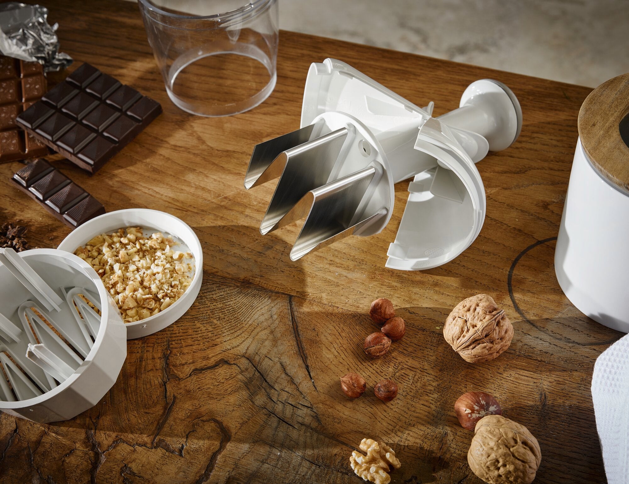Uien- en groentenhakker op een houten tafel, omringd door noten en chocolade. De hakmolen heeft scherpe messen en is ideaal voor het hakken van ingrediënten.