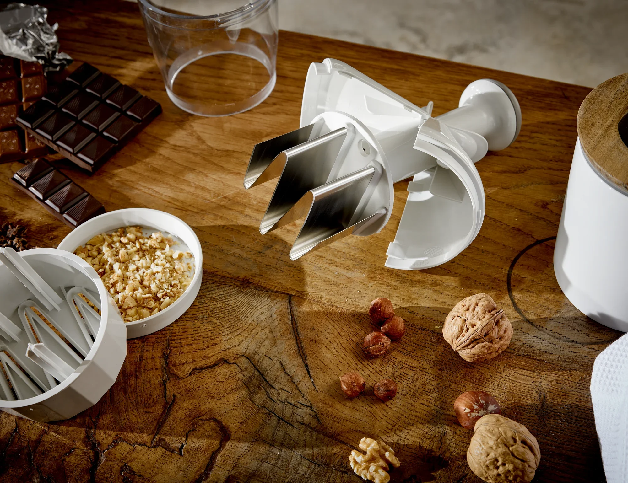 Zwiebel- und Gemüsehacker auf einem Holztisch, umgeben von Nüssen und Schokolade. Der Hacker hat scharfe Klingen und ist ideal zum Zerkleinern von Zutaten.