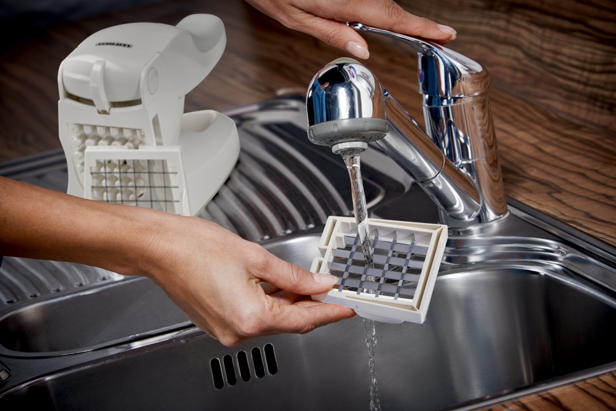 Der Leifheit Pommes-Frites-Schneider wird am Spülbecken gereinigt, während ein Gittereinsatz unter fließendem Wasser abgespült wird; die Anwendung zeigt einfache, hygienische Pflege im Küchenalltag.