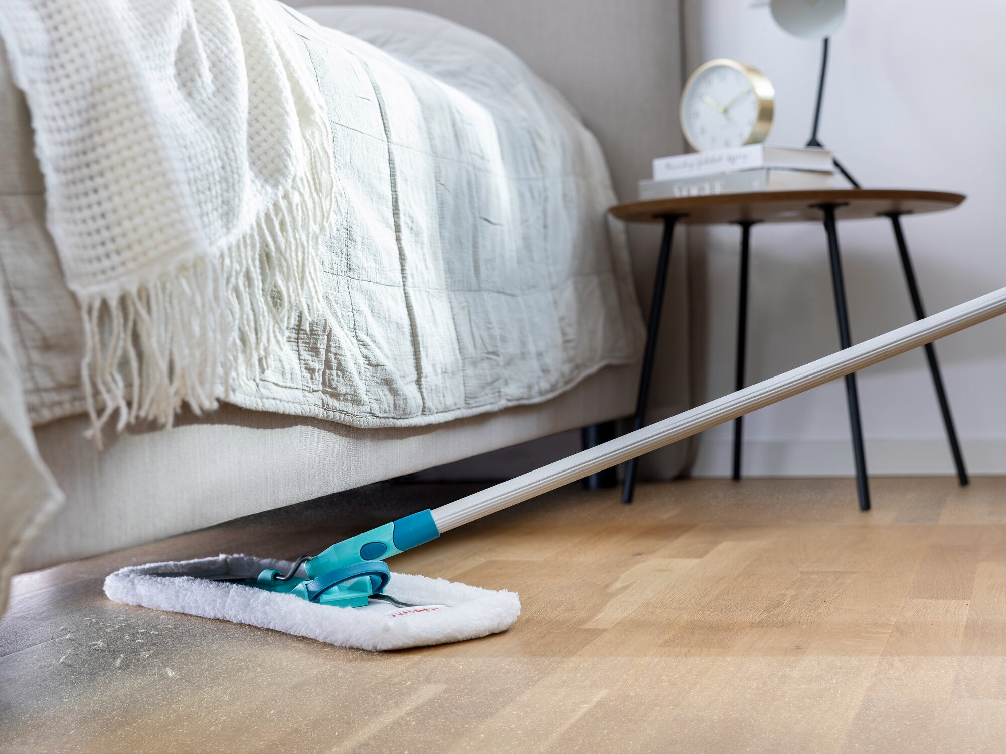 Ein SUPERDUSTER Staubwischer reinigt den Boden unter einem Bett. Der Wischer hat einen langen Griff und ein weißes Reinigungspad, ideal für schwer zugängliche Stellen.