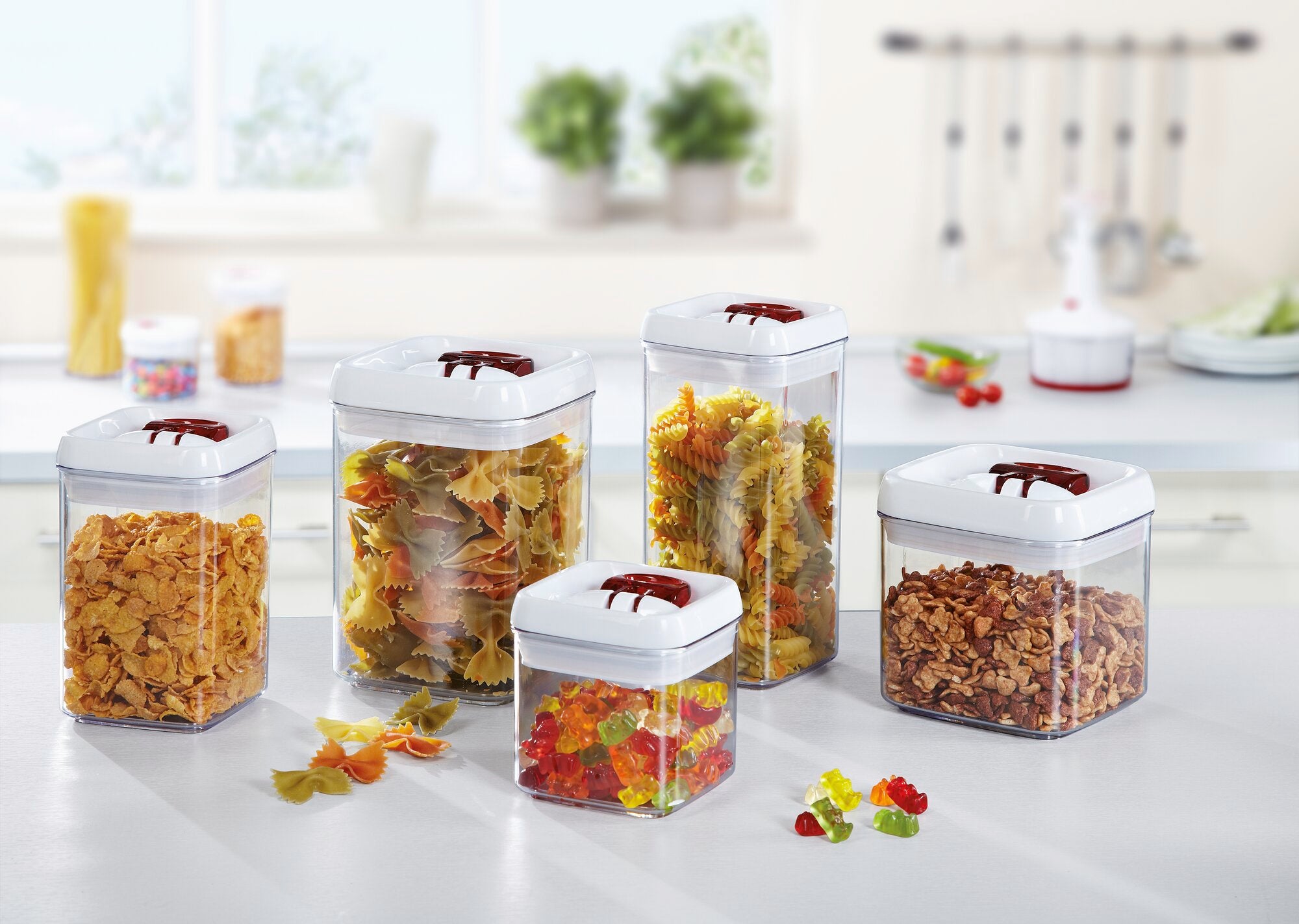 Set of transparent plastic storage jars in various sizes, filled with pasta, cornflakes and sweets. Ideal for storage in the kitchen.