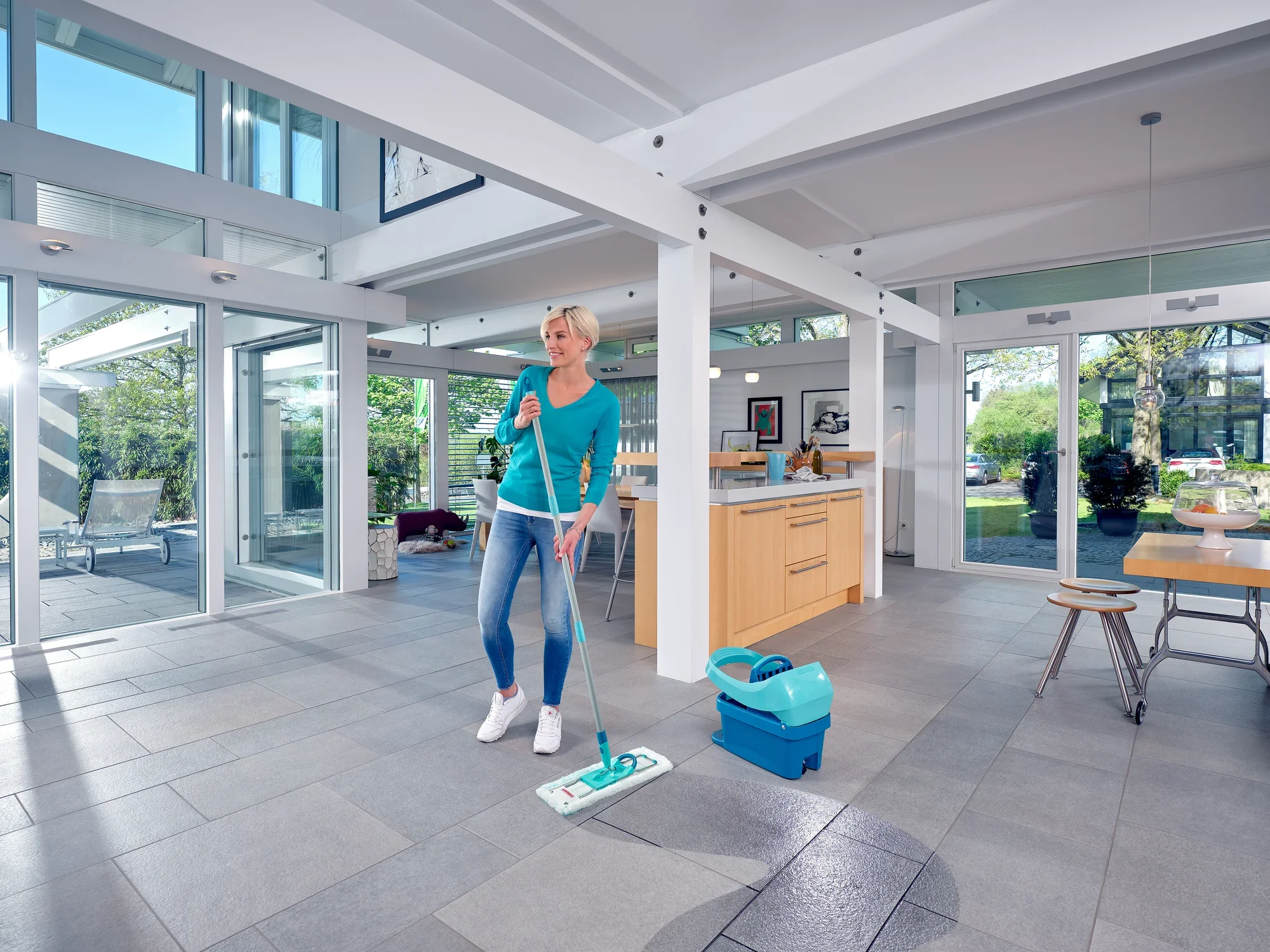 In een moderne, lichtovergoten kamer gebruikt een vrouw de Profi XL set met vloerwisser. De vloerreiniger is klaar om de vloer efficiënt schoon te maken.