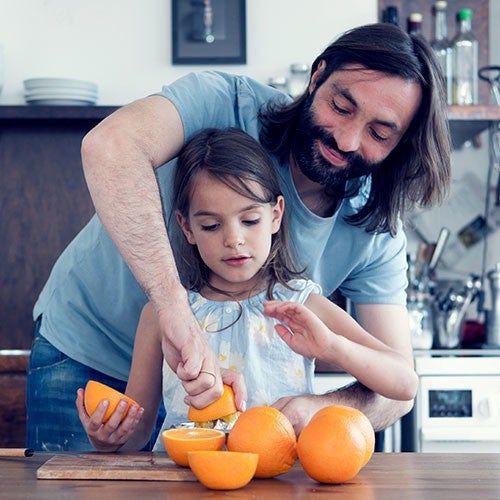 Un homme souriant aide une fillette a presser une orange dans une cuisine moderne, transformant des oranges en jus frais.