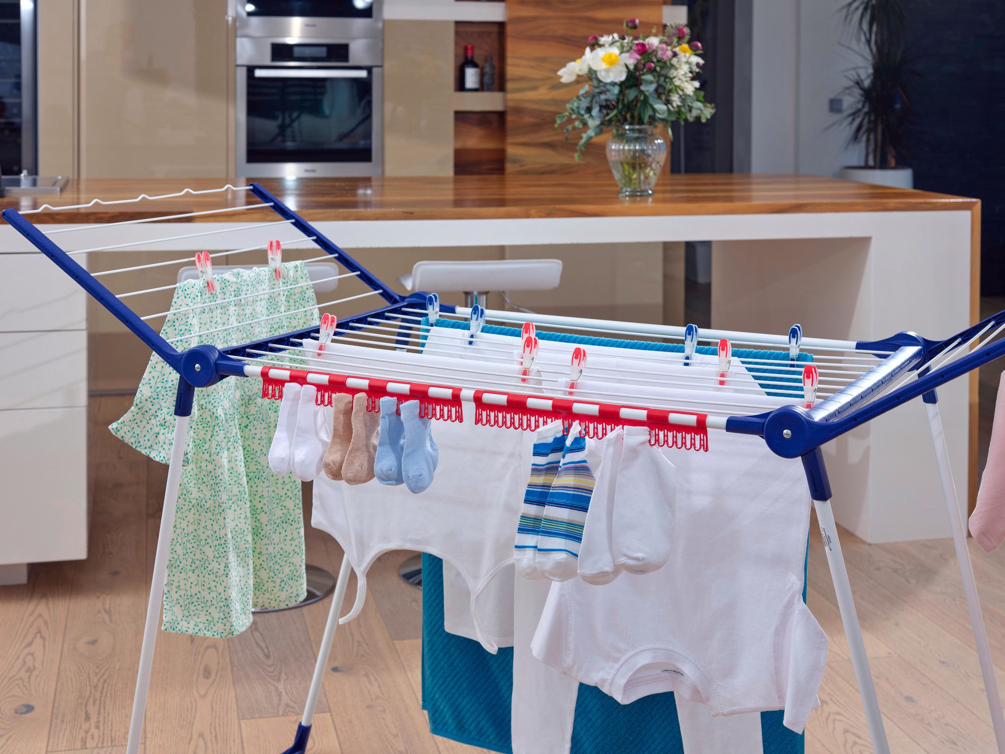 Ein Kleinteilehalter auf einem Wäscheständer in einer modernen Küche. Der Halter ist mit verschiedenen kleinen Kleidungsstücken wie Socken und Tüchern bestückt.