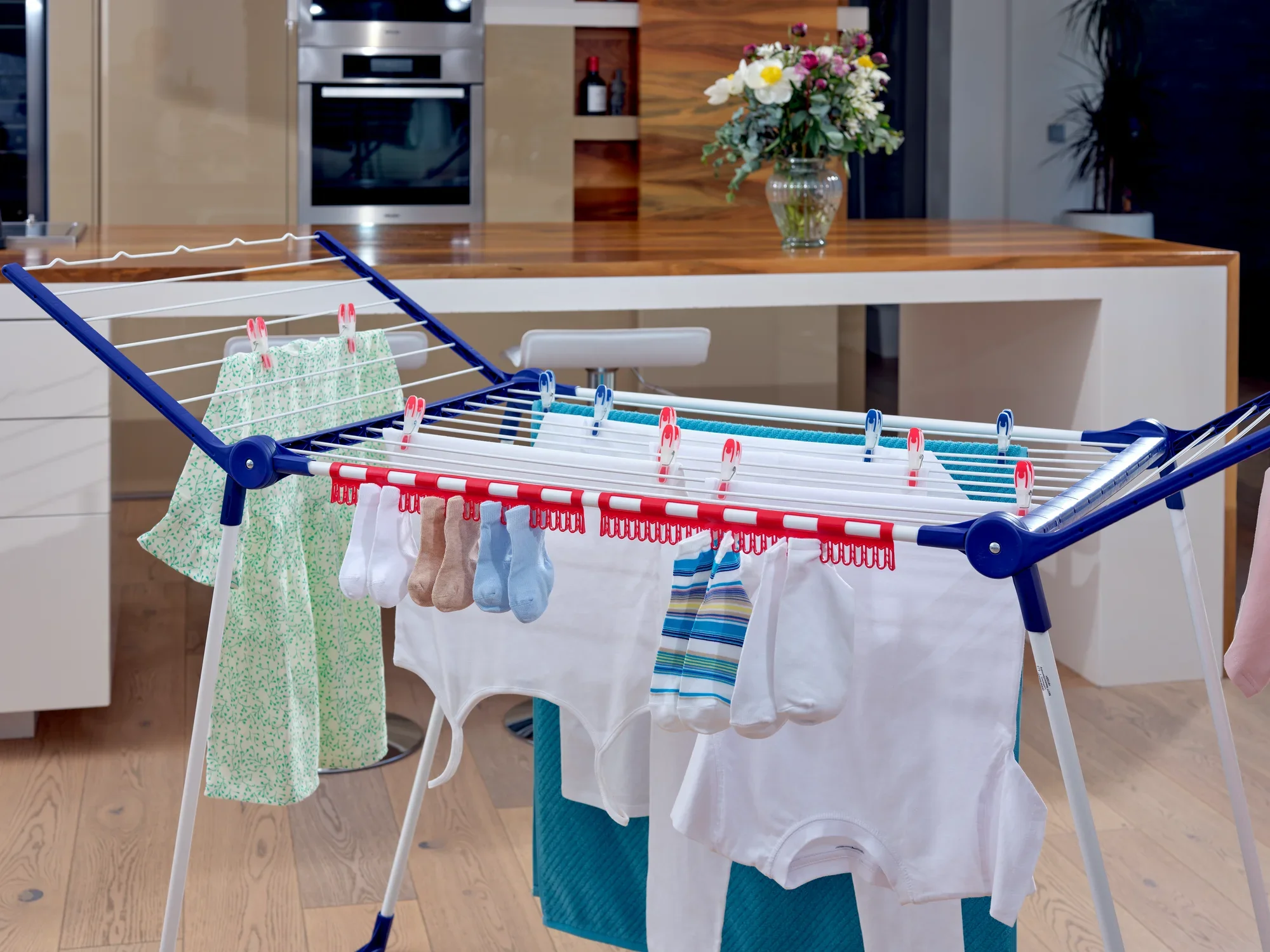 Ein Kleinteilehalter auf einem Wäscheständer in einer modernen Küche. Der Halter ist mit verschiedenen kleinen Kleidungsstücken wie Socken und Tüchern bestückt.