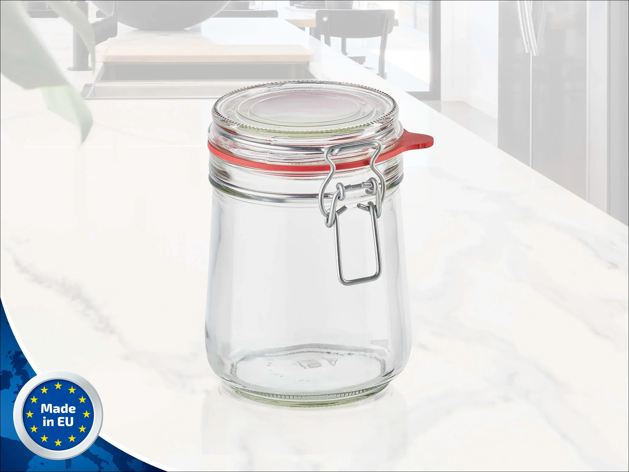 Drahtbügelglas von Leifheit mit einem Fassungsvermögen von 800 ml. Das Glas hat einen roten Gummiring und einen Metallverschluss. Ideal zum Aufbewahren von Lebensmitteln. Im Hintergrund ist eine moderne Küche zu sehen. Made in EU.